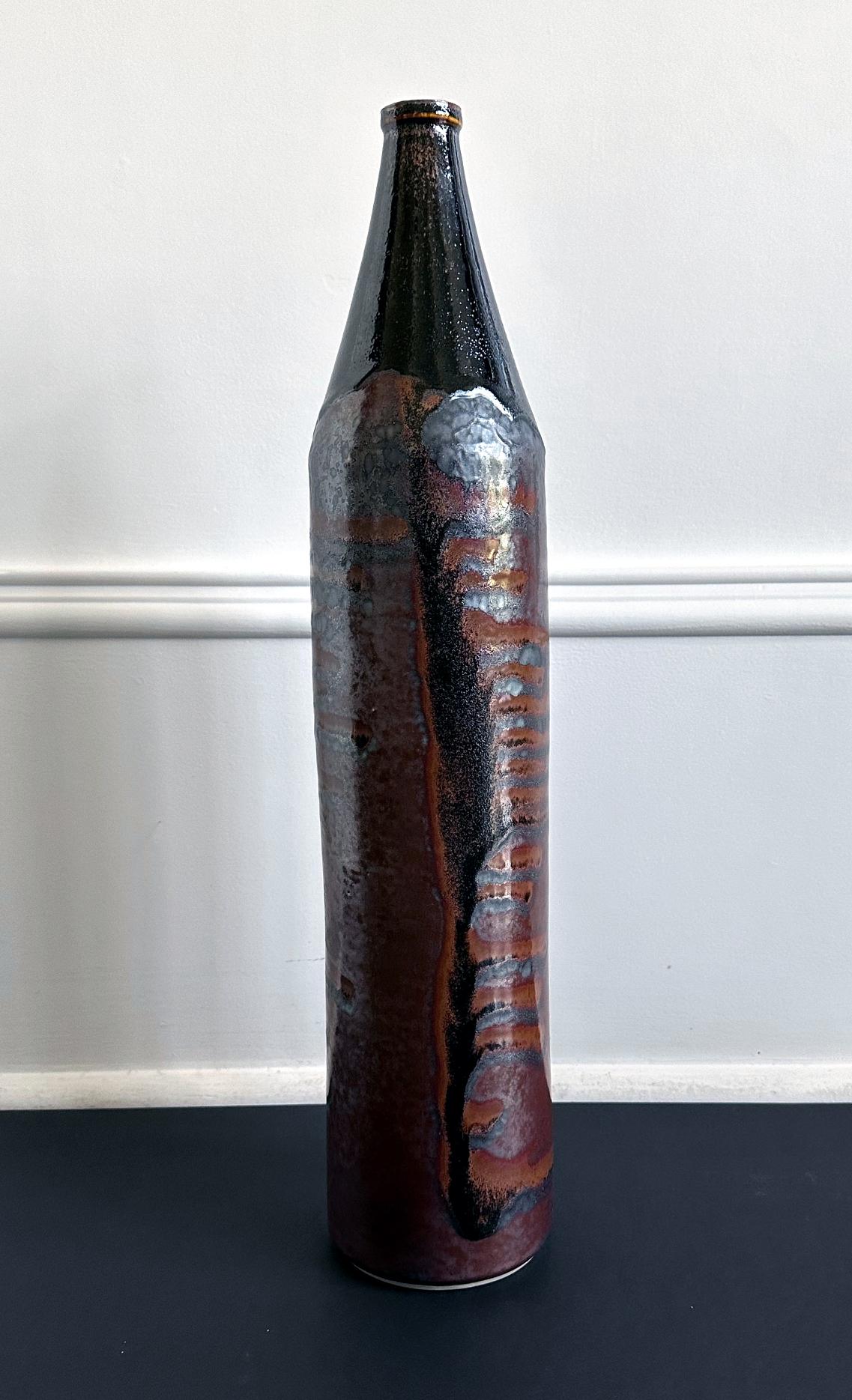 Un vase précoce en céramique de forme cylindrique du potier Frère Thomas Bezanson (1929-2007). D'une hauteur inhabituelle de 21,75 pouces, le vase frappe l'observateur par sa silhouette élancée, avec un col effilé et une ouverture en forme de
