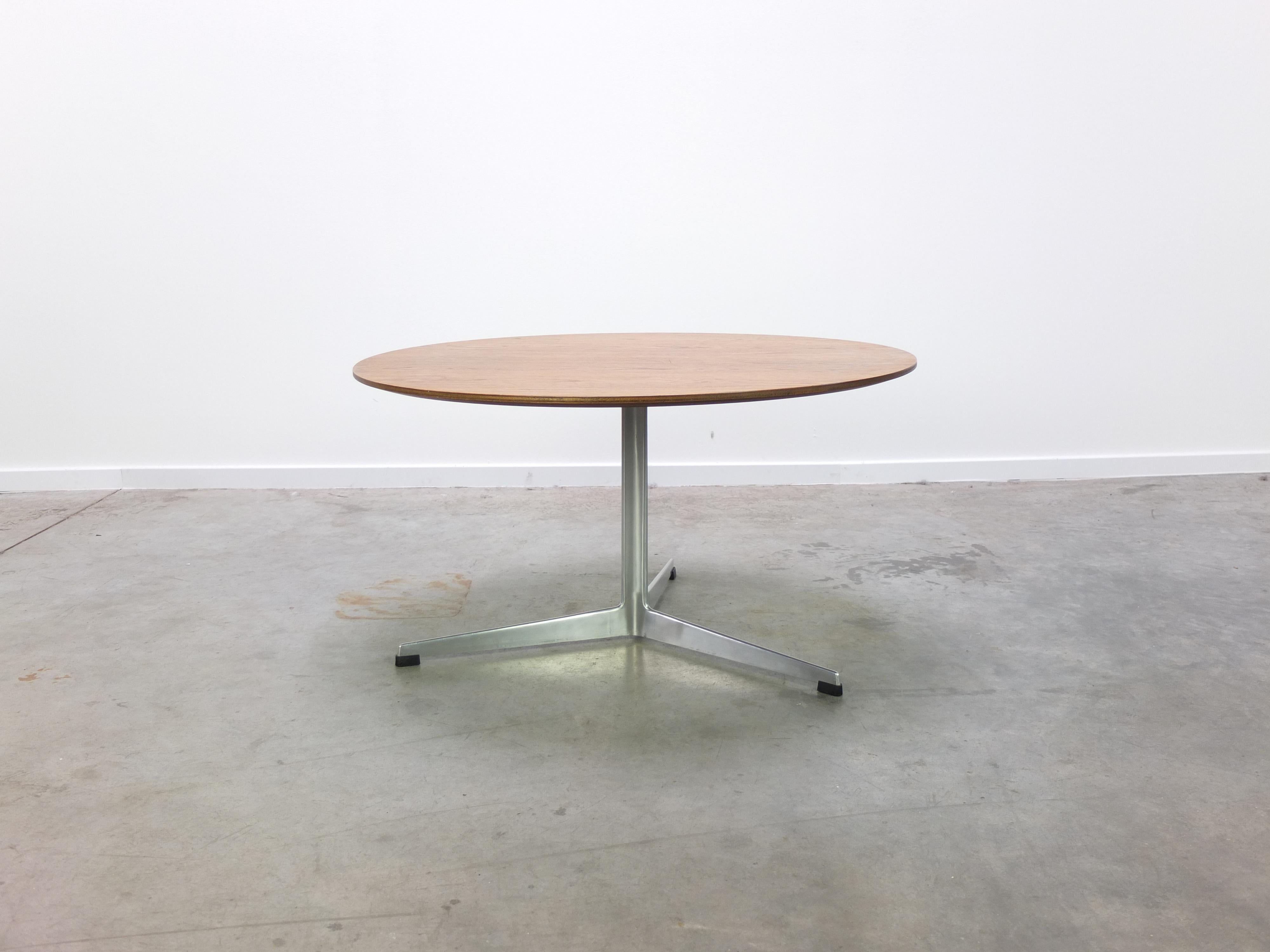 Magnifique table basse ronde conçue par Arne Jacobsen dans les années 1960. Le plateau est en bois de teck et repose sur la base centrale en aluminium à trois pieds. Produit au Danemark par Fritz Hansen en 1964 (labellisé). En très bon état