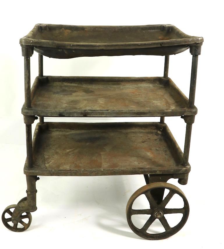 Nice early Industrial cart having a tubular iron frame, cast iron wheels, and steel shelves. The cart is structurally sound and sturdy, it shows significant cosmetic wear, normal and consistent with age and use. The shelves dip in the middle