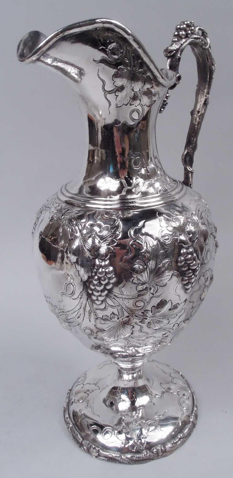 Tall Classical sterling silver wine ewer. Made by Moore for Tiffany & Co. at 550 Broadway, New York, ca 1855. Ovoid bowl with helmet mouth and raised round foot; cast high-looping fruiting grapevine handle. Foot rim encircled with same. Chased and