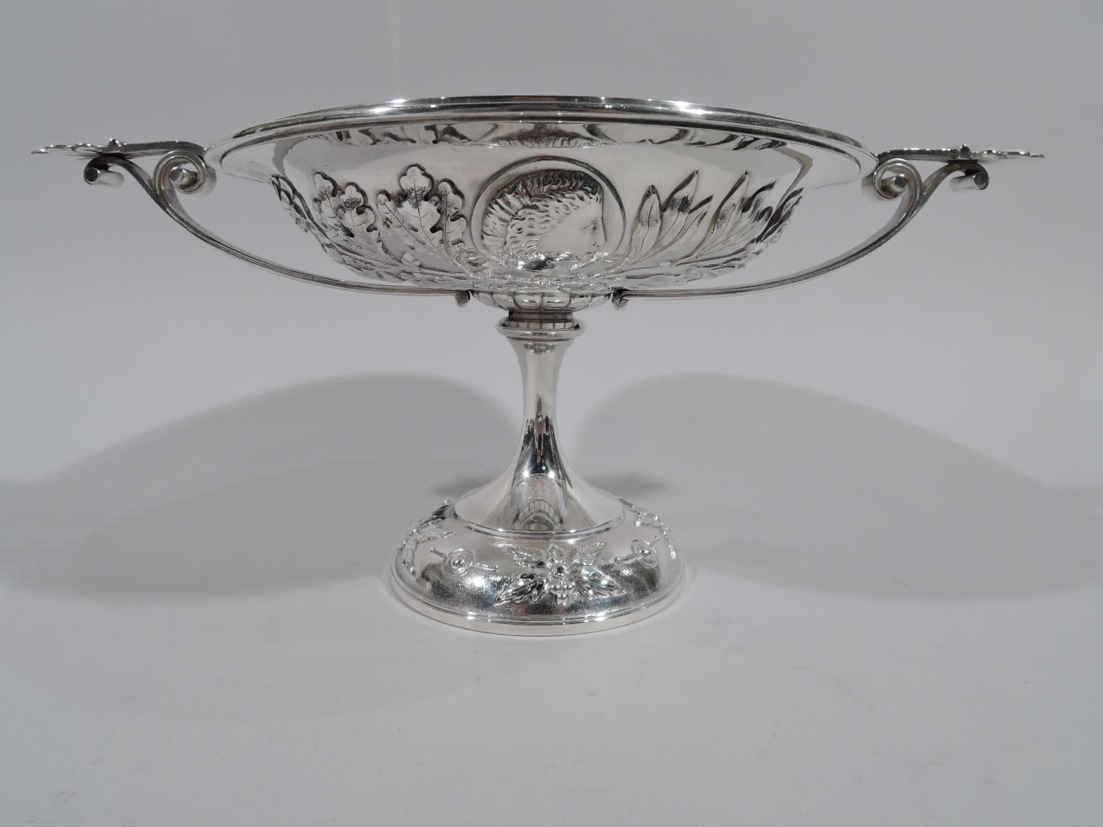 Greek Revival sterling silver footed bowl. Made by Grosjean & Woodward for Tiffany & Co. at 550 Broadway in New York. Bowl wide and shallow with flat fretwork rim. Ornament applied to exterior: Medallions inset with male youth heads surrounded by