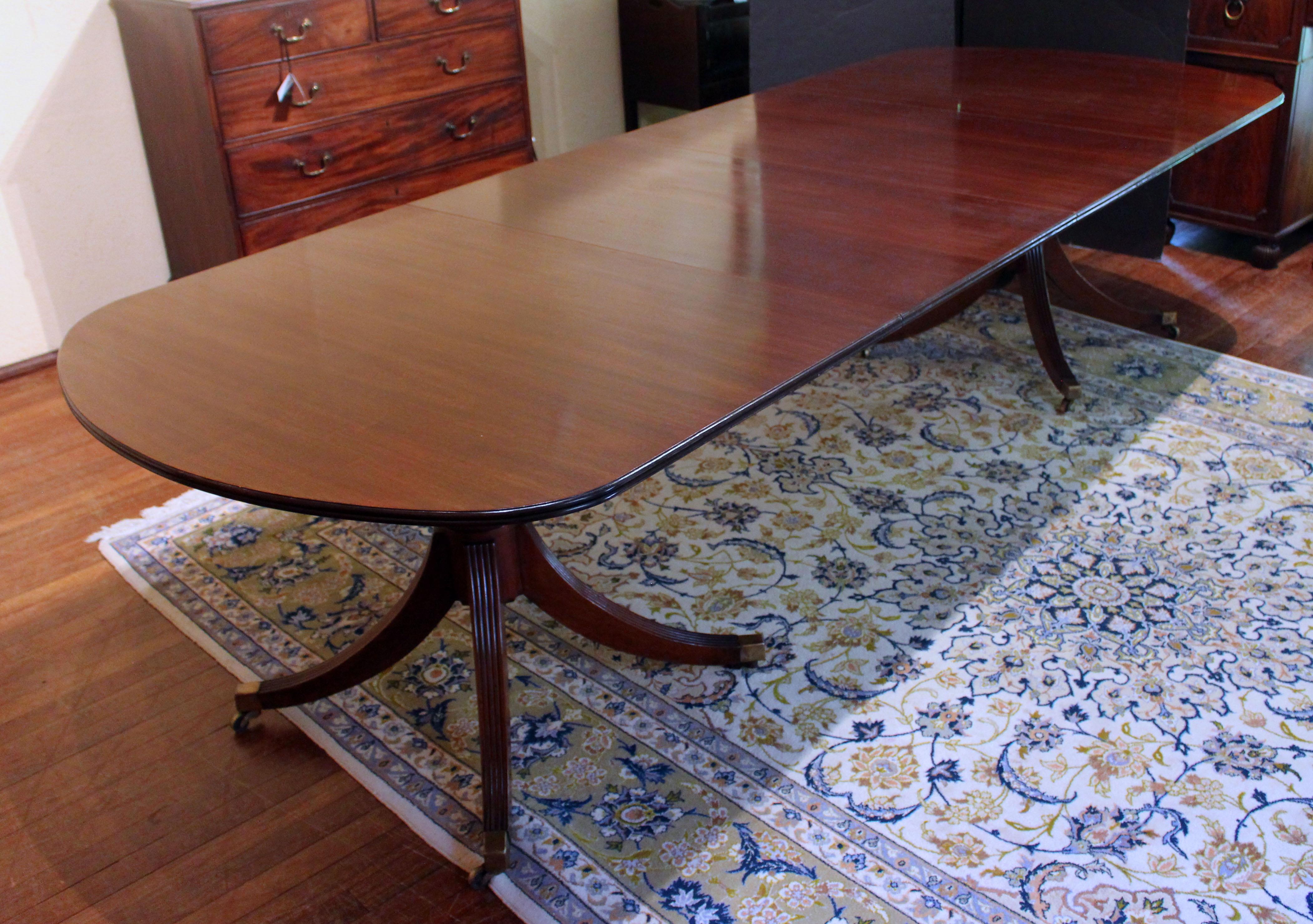 Table de salle à manger anglaise à double piédestal du début au milieu du 20e siècle. Bois d'acajou riche et de haute qualité et artisanat. Deux feuilles. Robuste plateau à double moulure qui est repris dans le tournage en anneau des fûts du