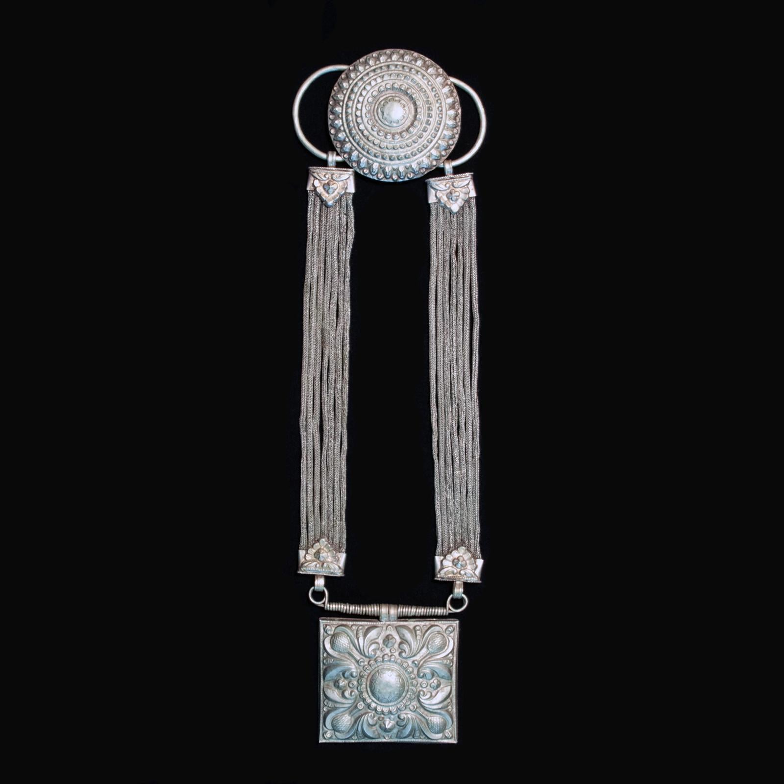 Early to mid-20th century Jantar necklace, Nepal

This long silver alloy (kakar-manka) necklace, a jantar, features a hollow repoussé square pendant, which is suspended from seven woven silver wire cords on each side, anchored in the back with a