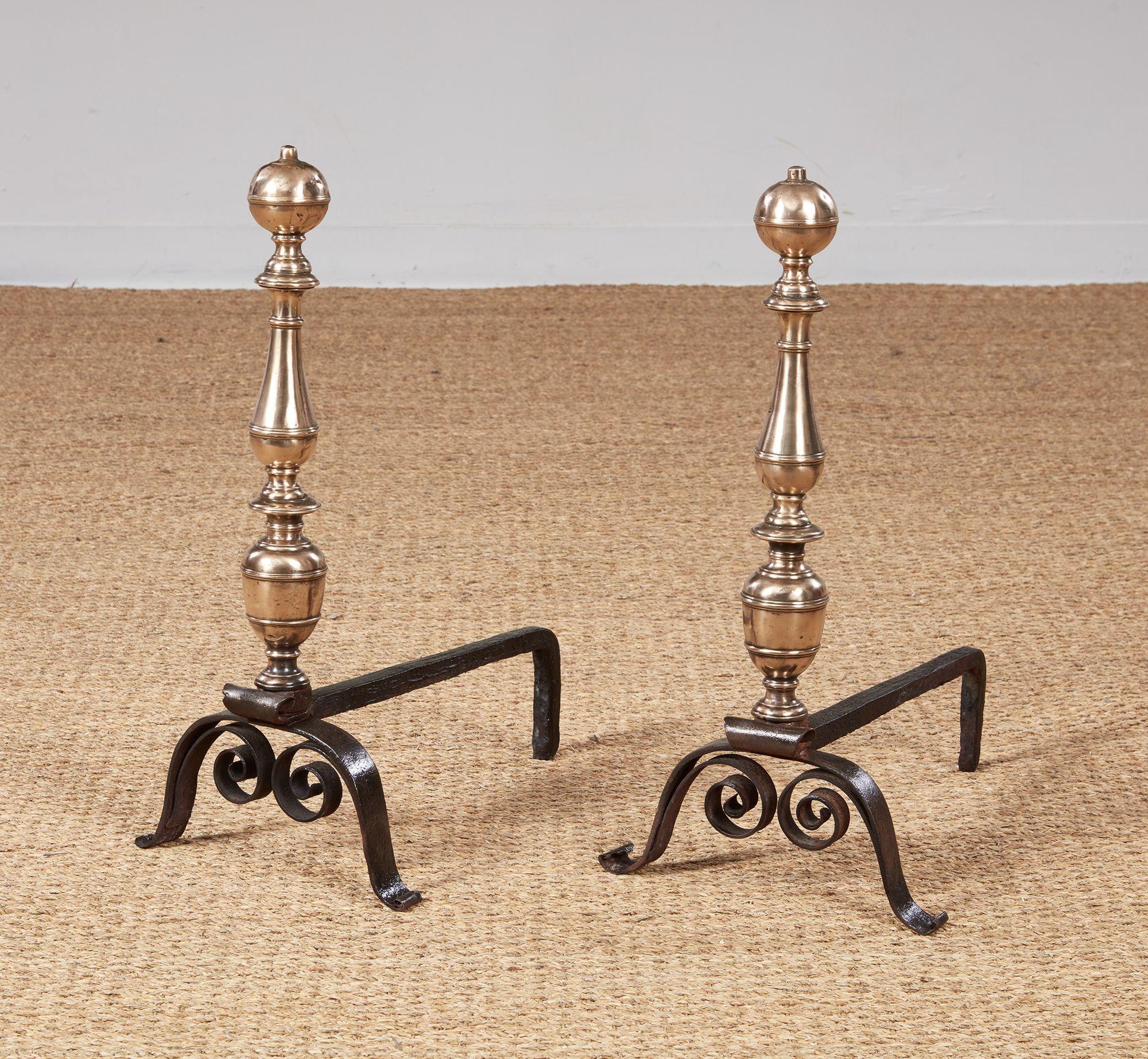 A delightful pair of early andirons with elaborately turned bronze shafts surmounted by ball tops and featuring wrought iron legs with underscrolls, also with wrought iron back supports.