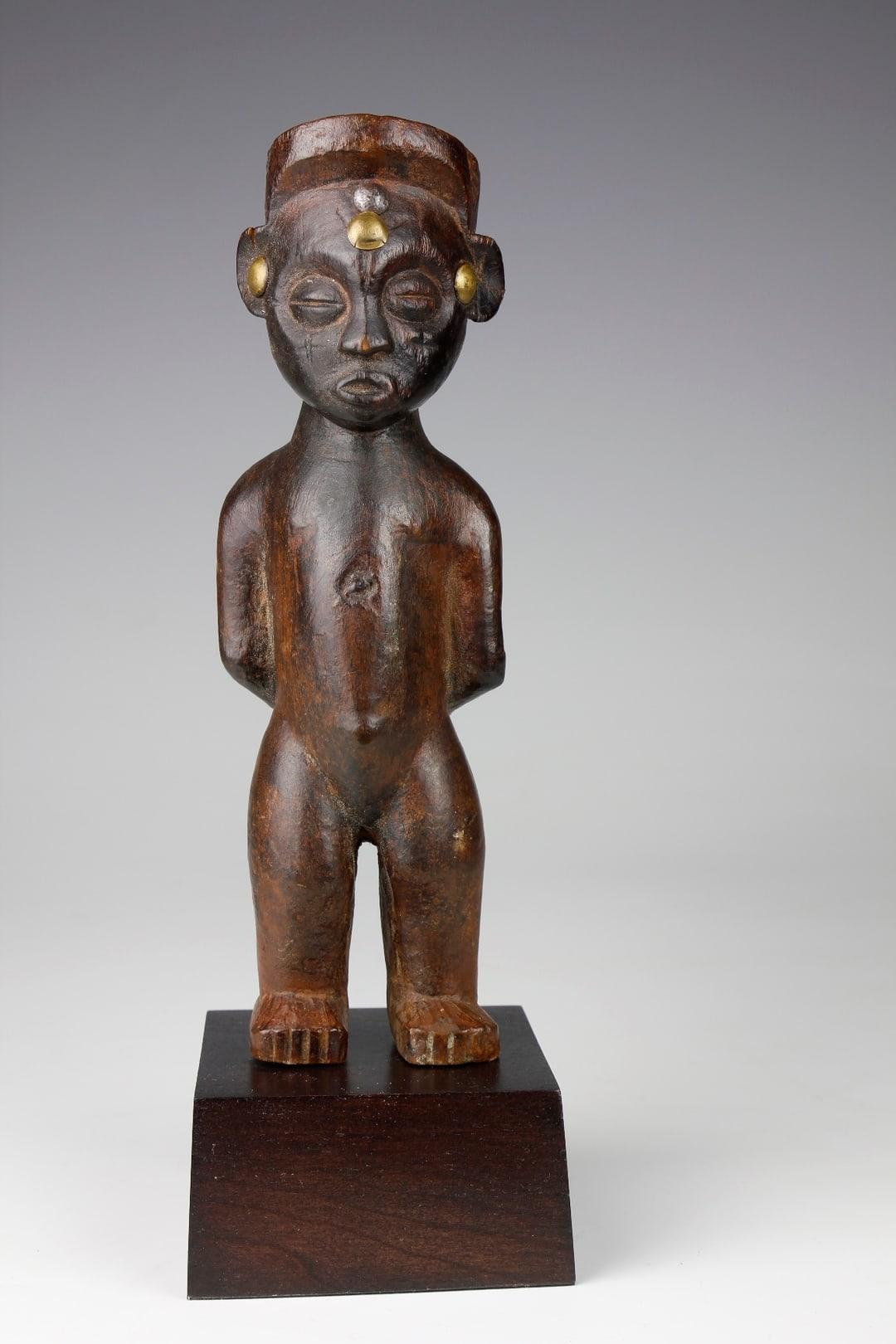 This early twentieth-century figurative sculpture, from the Lwena/Chokwe culture in the Angola-Zambia Border Region, depicts a female standing in an upright stance. 

A defining characteristic of this piece is the position of the female's arms,