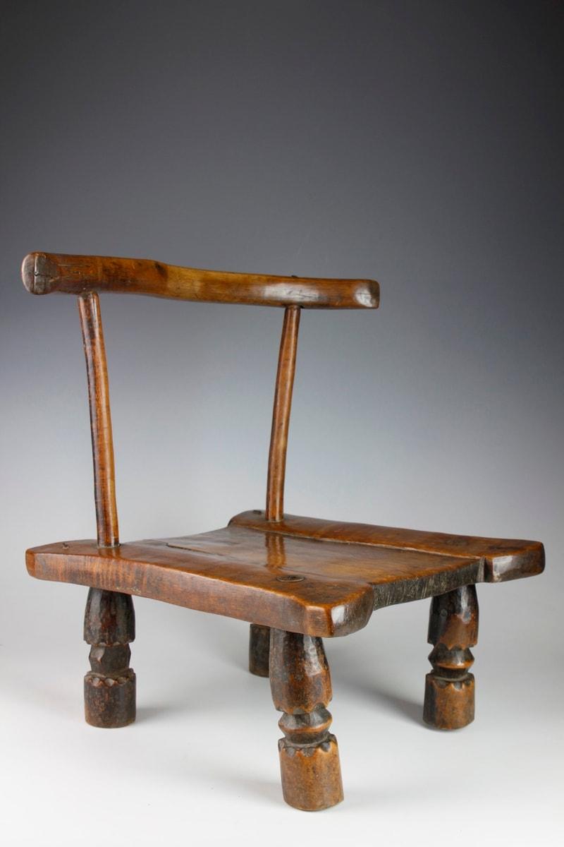 This early twentieth-century small chair displays a beautiful form. Typically low to the ground, such chairs are found among the Dan and Baule cultures in the Ivory Coast. Carved from a hard brown wood, the chair consists of a curved back support