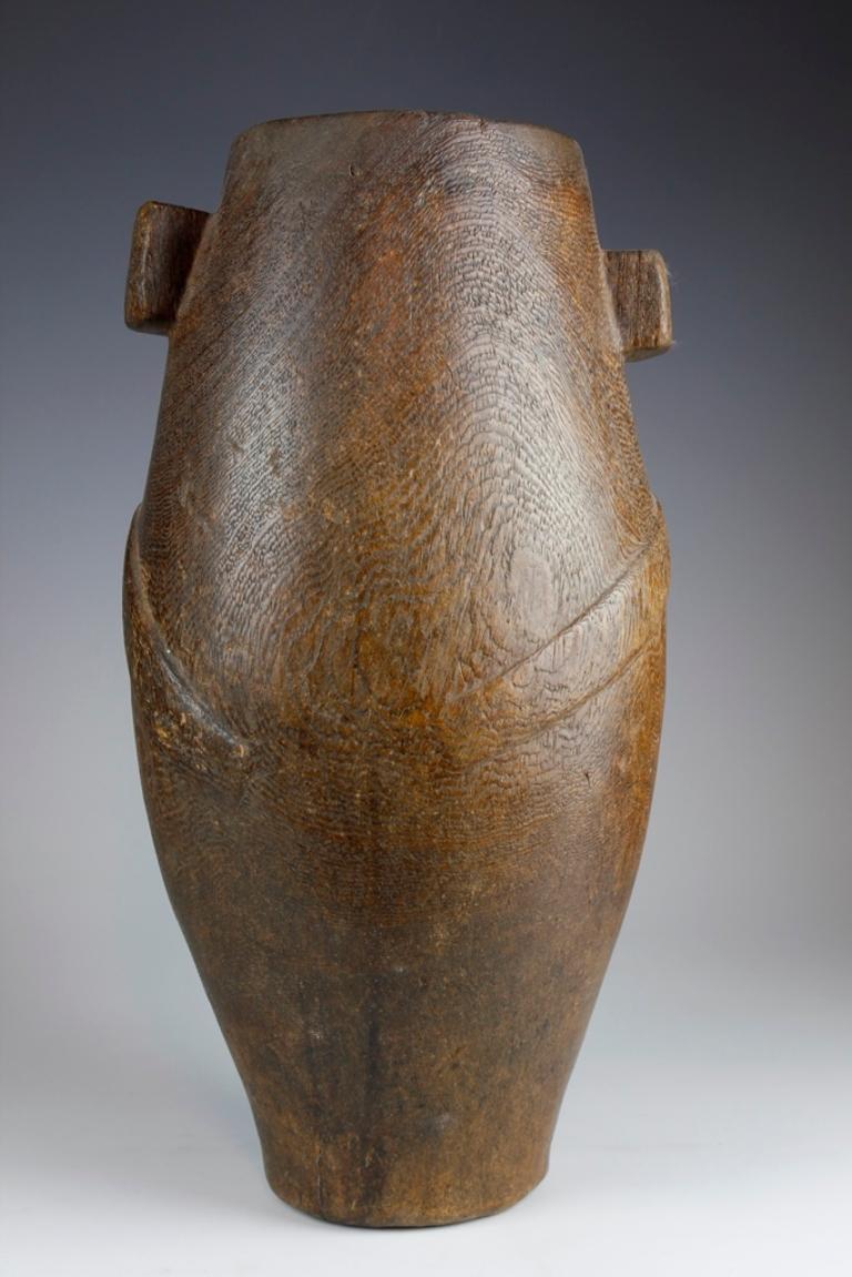 This early-twentieth-century tall, narrow vessel, from the Zulu culture in South Africa, would have traditionally served as a milk pail. 

Known as an 'ithunga', the vessel exhibits a lovely curving form, with two carved wooden rectangular lugs on
