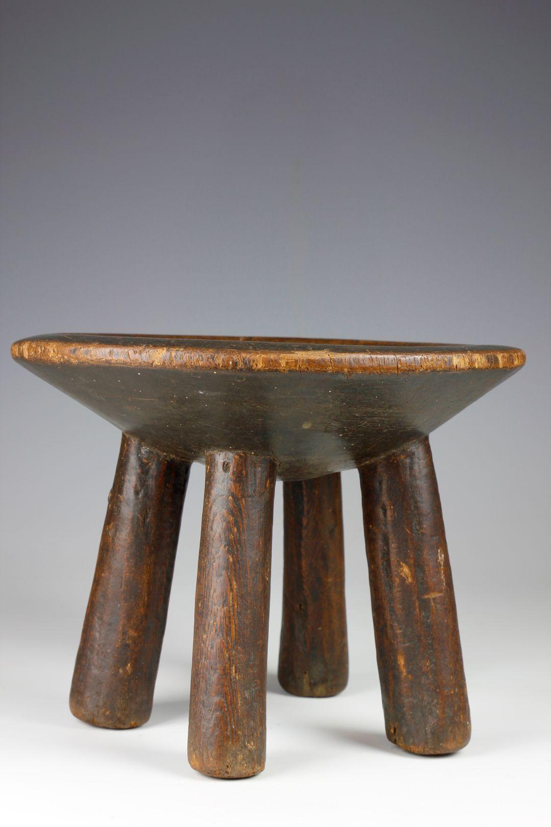 The form of this finely carved early twentieth-century village stool, from the Hehe culture in Tanzania, consists of four short, upright legs supporting a dish-shaped seat. A small decorative metal stud adorns one of the legs and over time, the