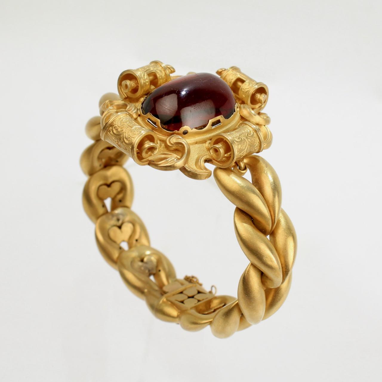 A very fine antique Victorian era 18K gold and garnet bracelet.

With a decorative scroll frame centered by a prong set oval garnet cabochon in 18k gold.  

Braided gold bands wrap around the wrist with a box clasp closure and a safety chain.  

The