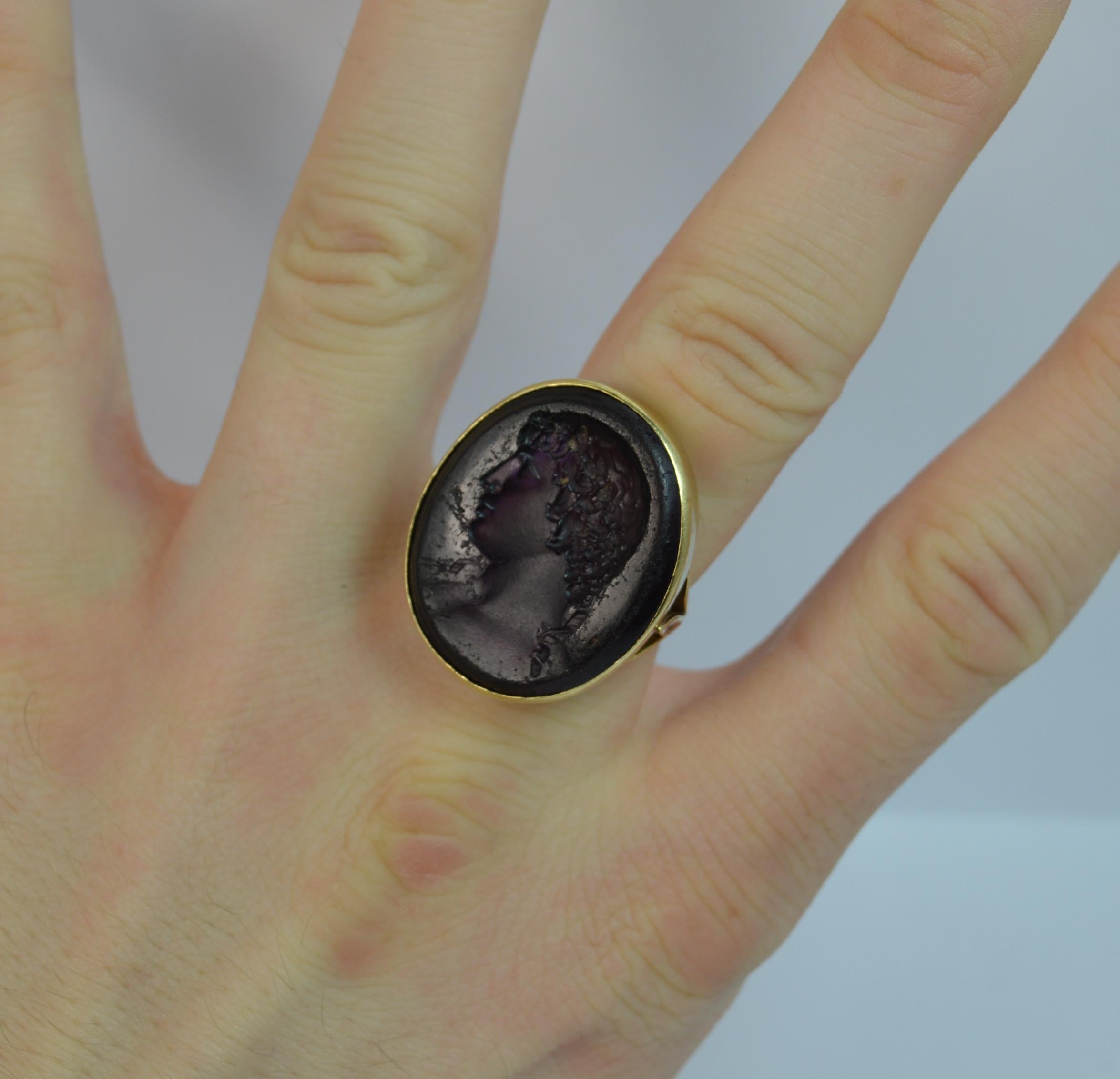 A stunning 18 carat gold and purple amethyst glass ring.
SIZE ; O 1/2 UK, 7 1/2 US
A signet seal intaglio ring. The face depicting a classical male bust of superb detail. 22mm x 26mm head.

Modelled onto a solid 18 carat yellow gold shank with fleur