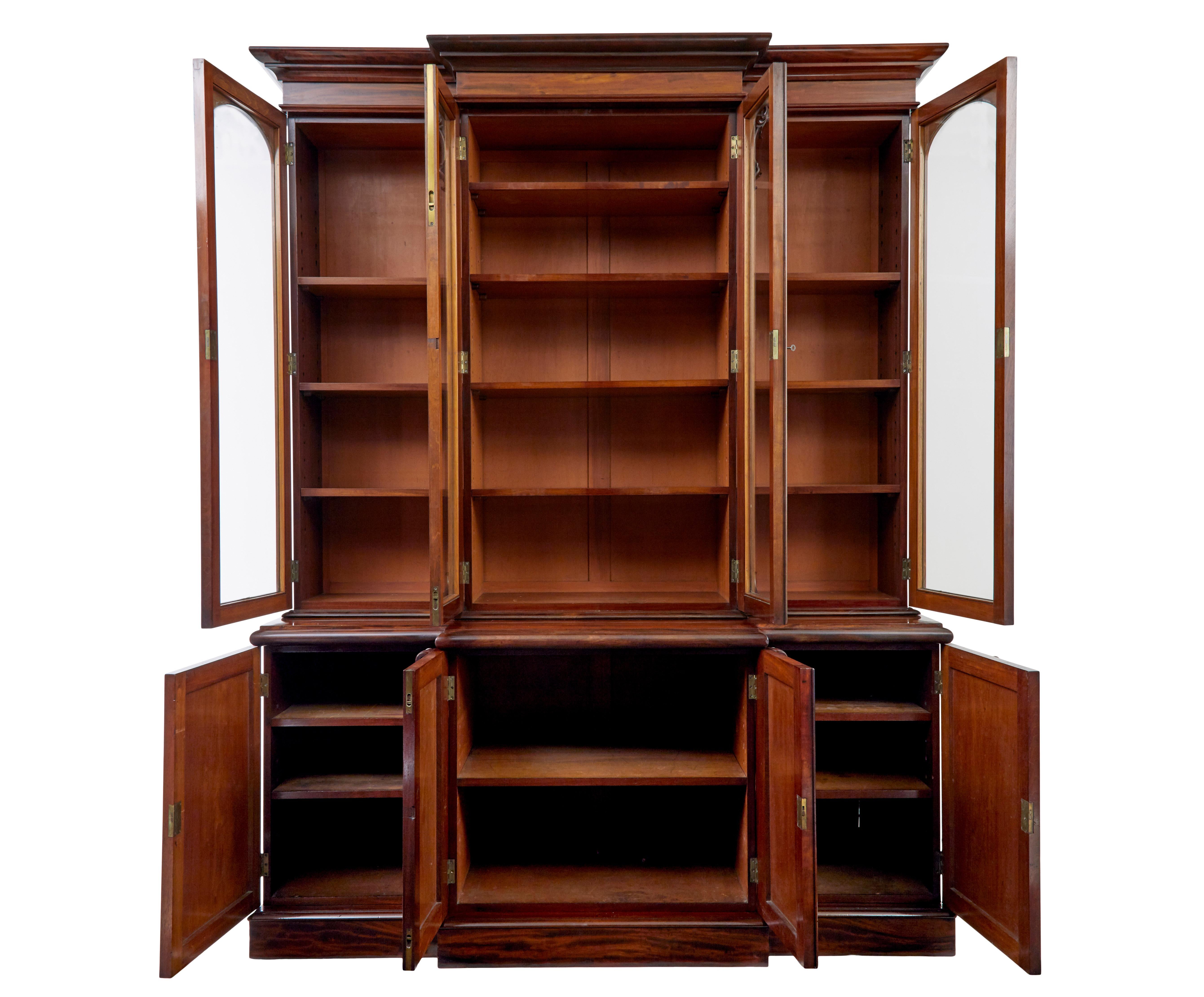 Early victorian 19th century flame mahogany breakfront bookcase, circa 1850.

Comprising of 5 sections. Plinth, cupboard, middle section, glazed unit and cornice.

Made front the finest quality matching veneers. With applied lambs tongue carvings.