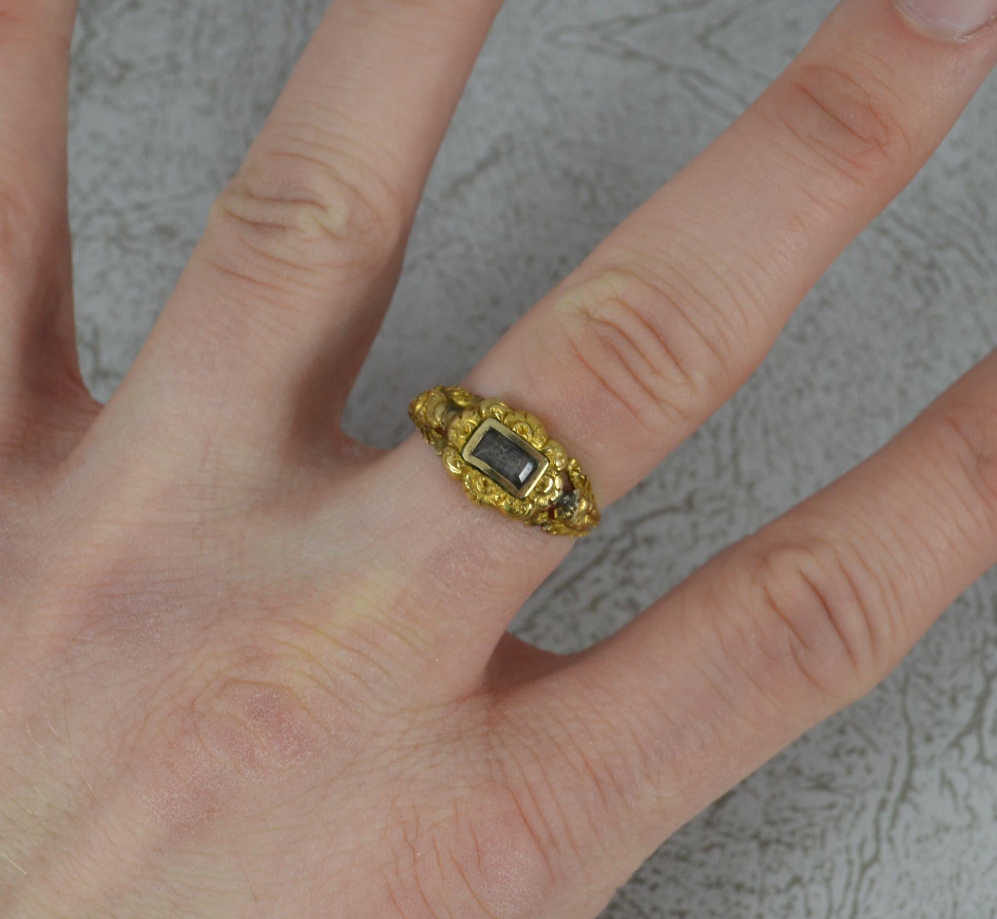 A very early Victorian period mourning ring.
Solid 22 carat yellow gold example.
Designed with a locket section to the centre with glass front. Fine floral chasing surround and to shoulders.
9.4mm wide band to the front.

CONDITION ; Good age age.