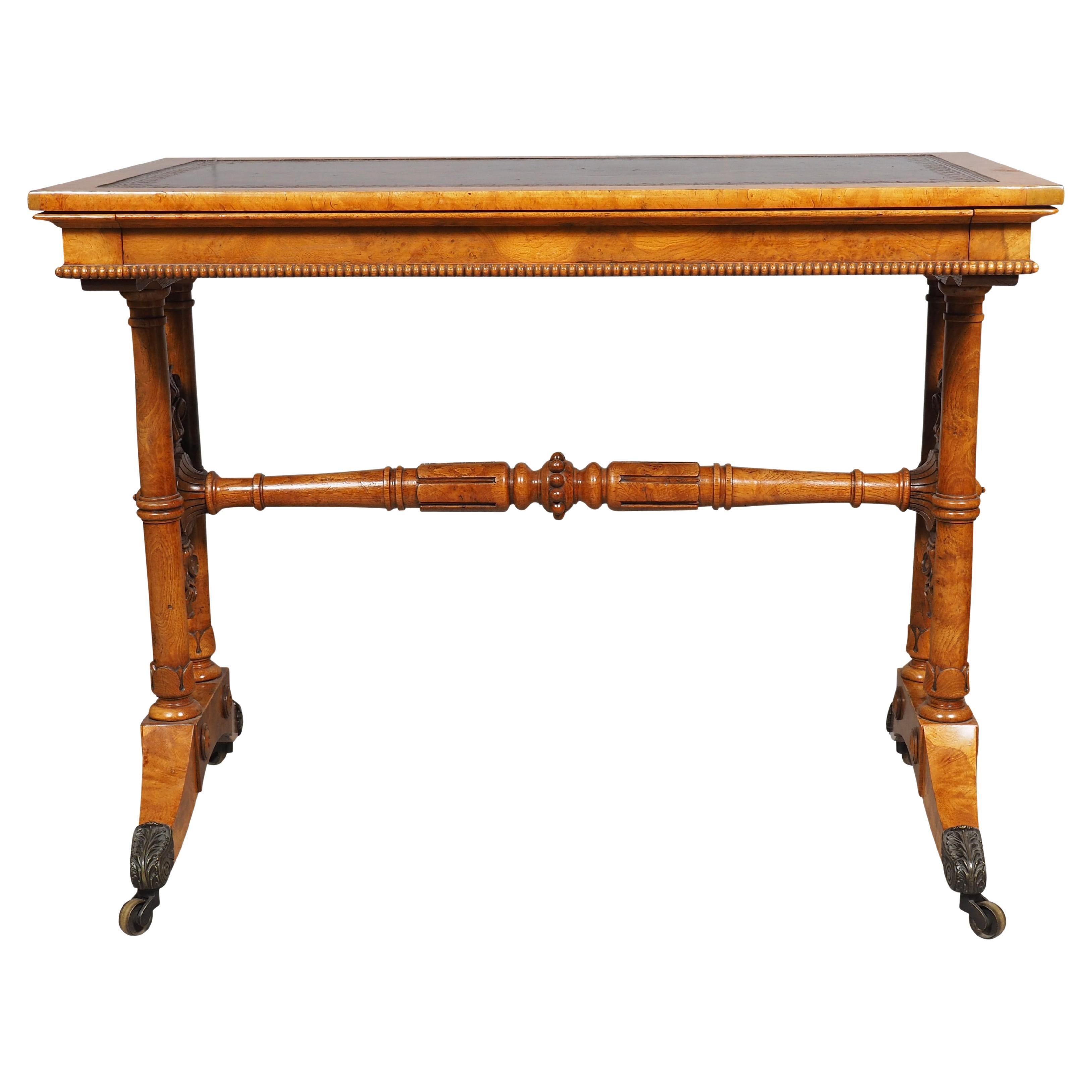 Rectangular top with maroon leather and  banded edge over a drawer raised on a trestle base with turned stretcher and carved ends. Saber legs with casters.