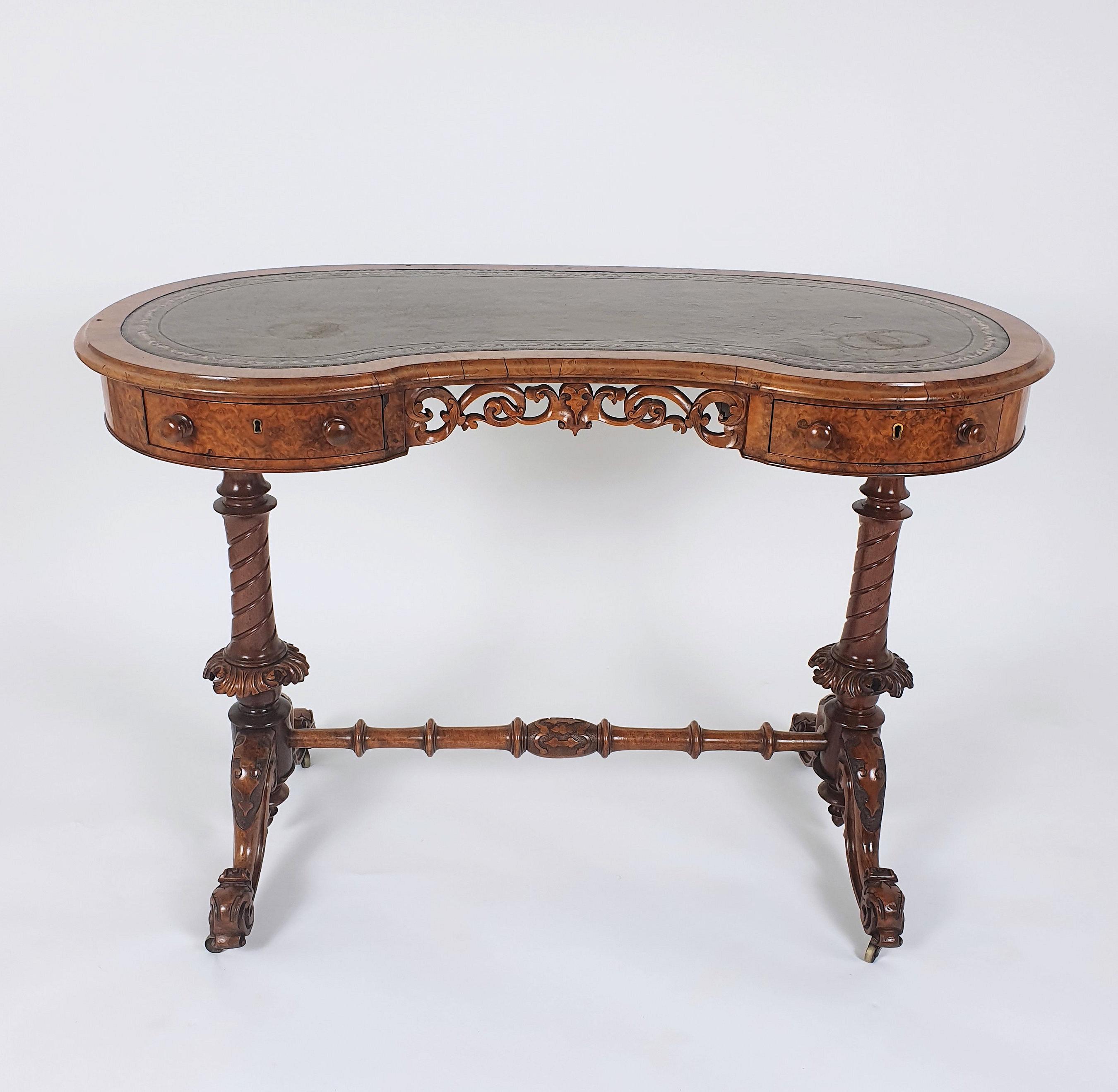 This exceptional early 19th century burr walnut ladies writing table features a kidney shaped top with the original leather inset and castors. The table has an ornately carved central knee hole flanked by 2 drawers with twin spiral turned supports
