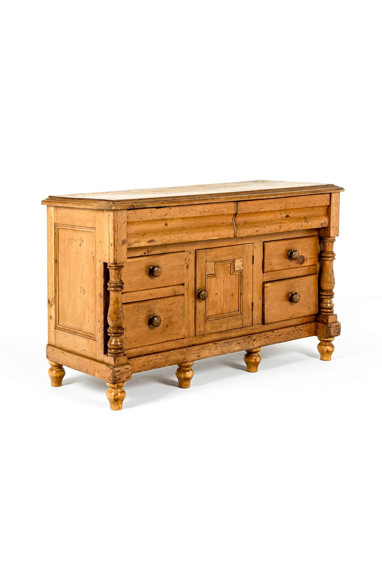 A superb early Victorian pine dresser base of compact form.

The moulded top has a gently stepped edge above two frieze drawers with original button handles.

Beneath a panelled cupboard with an arrangement of four smaller drawers flanked by a pair