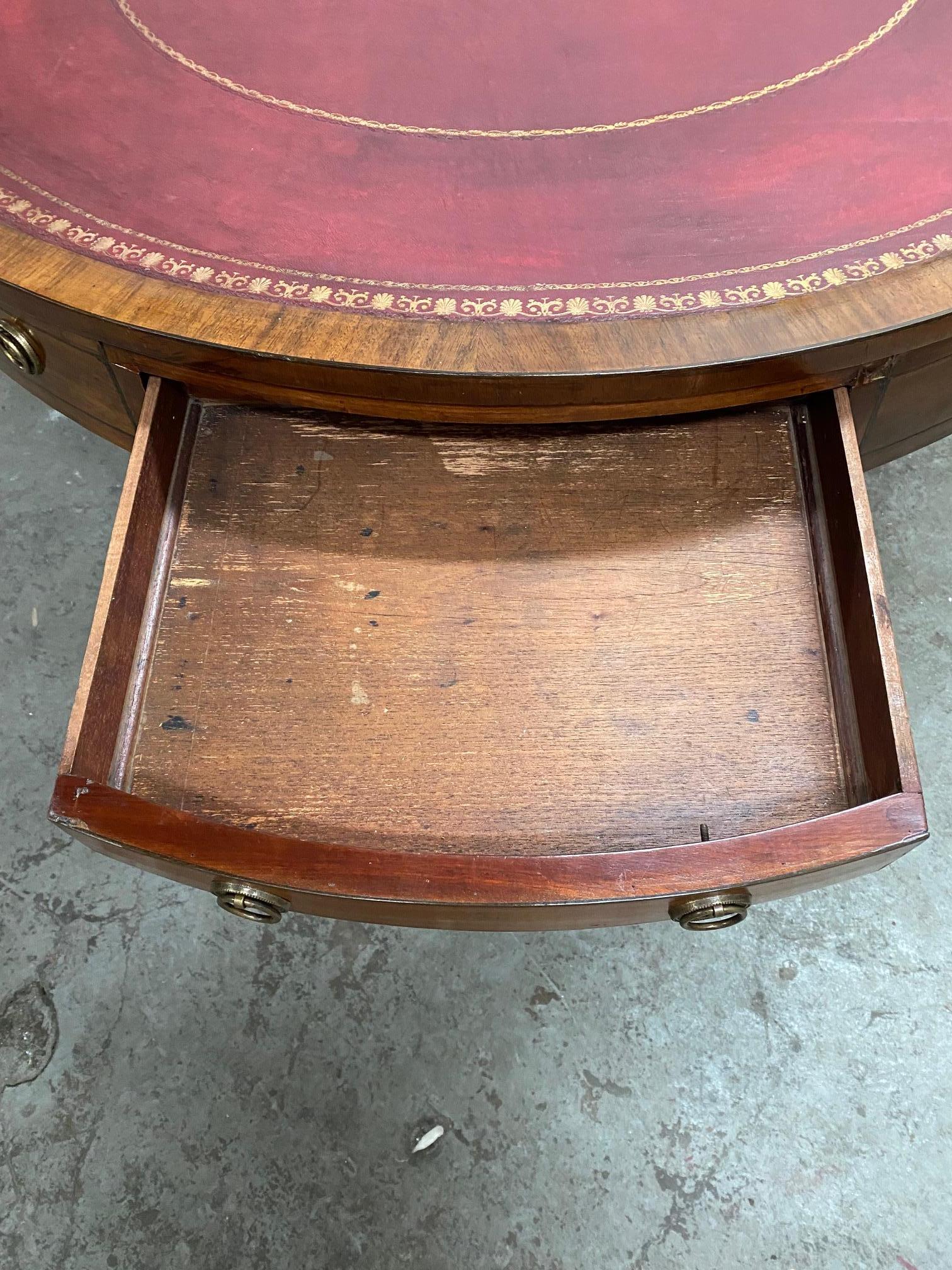 English mahogany drum table inset with red gilt tooled leather resting on tripod base.
 