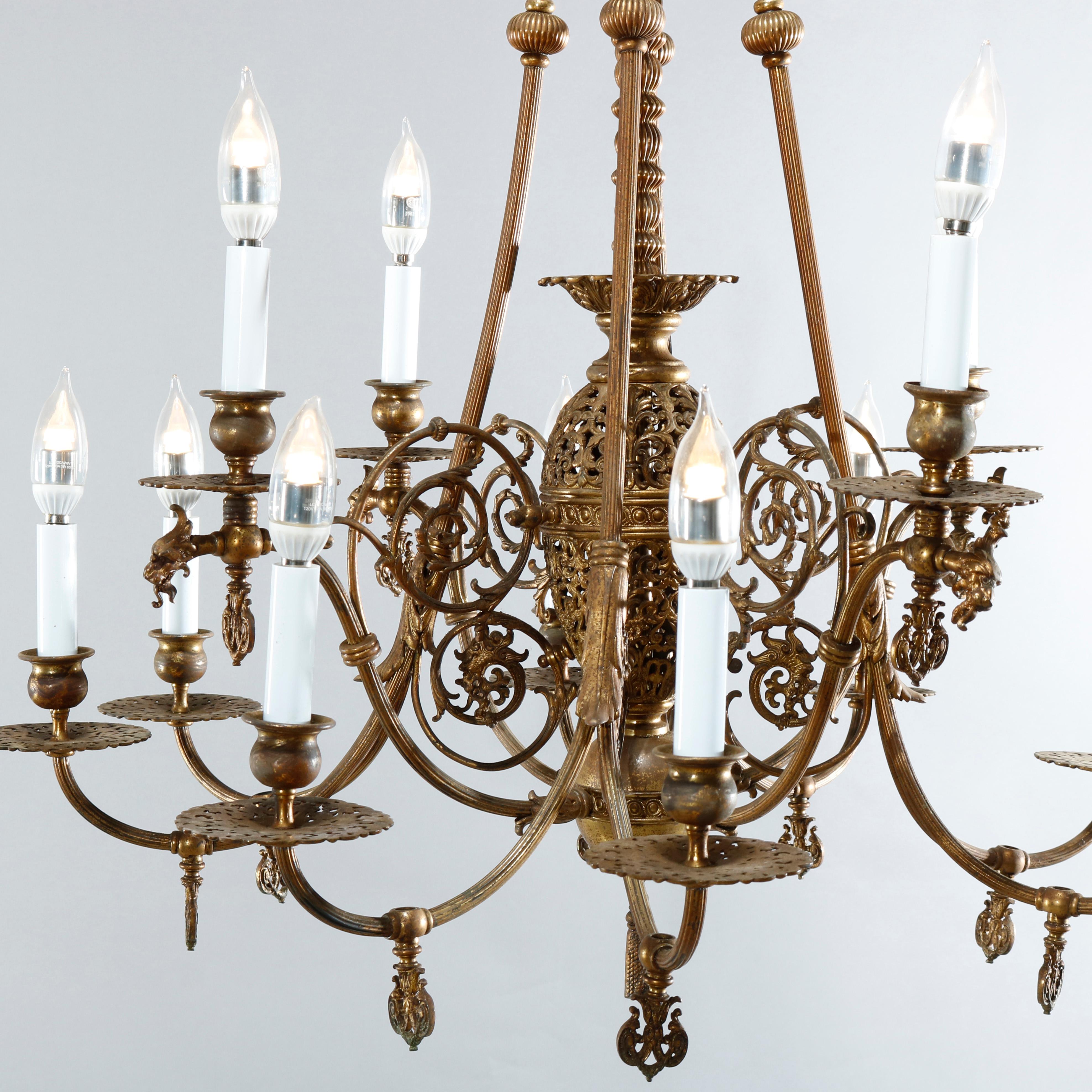 An early Victorian combination gas and electric chandelier offers brass and bronze construction with foliate filigree font having scroll and foliate form and reeded arms terminating in twelve candle lights, drop pendant and acanthus elements
