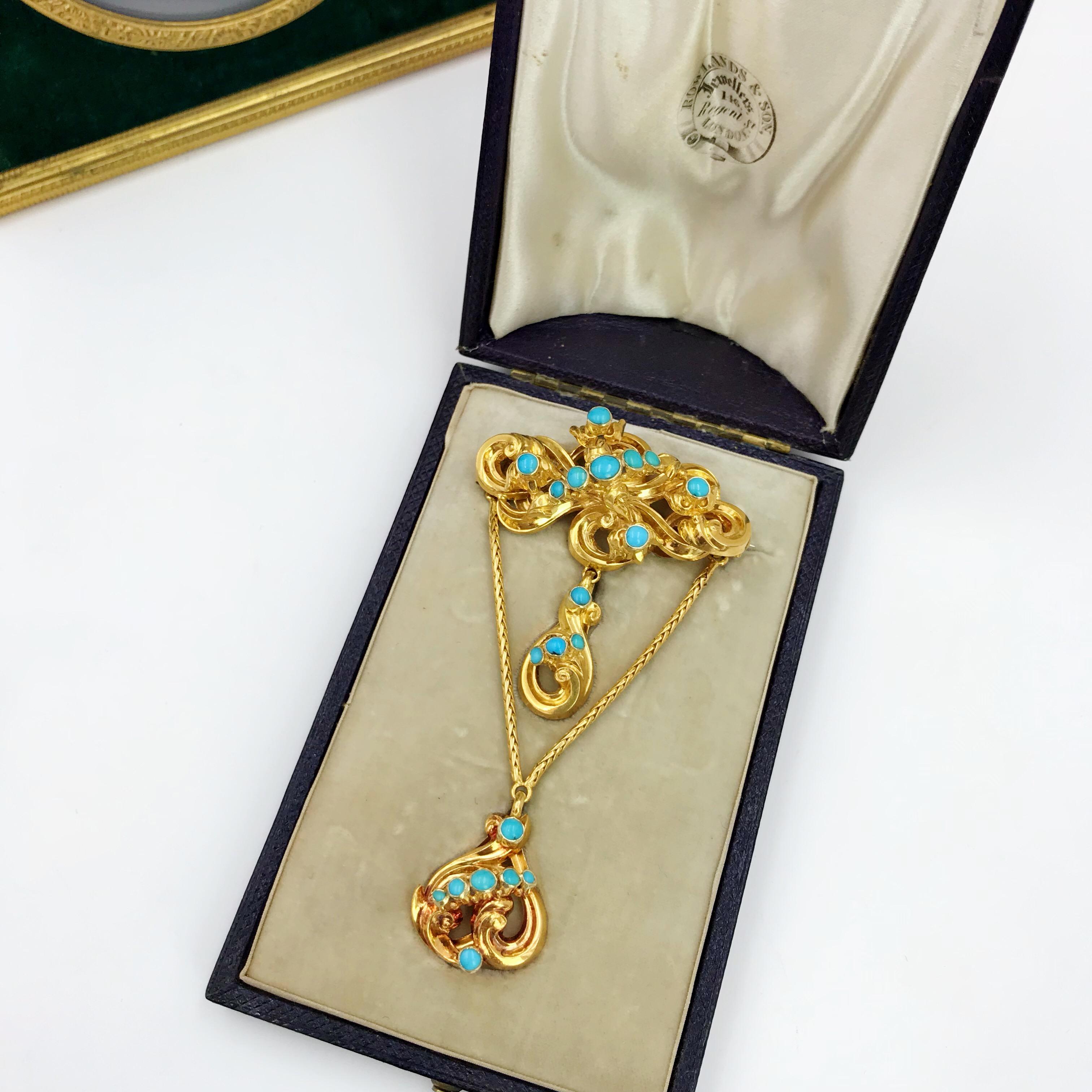 An early Victorian gold turquoise sentimental brooch. Comprising a grooved scroll, with turquoise cabochon floral highlights, suspending a similarly-designed drop and further drop on snake-link swag. Length 8cms. Weight 11gms. With fitted case.
