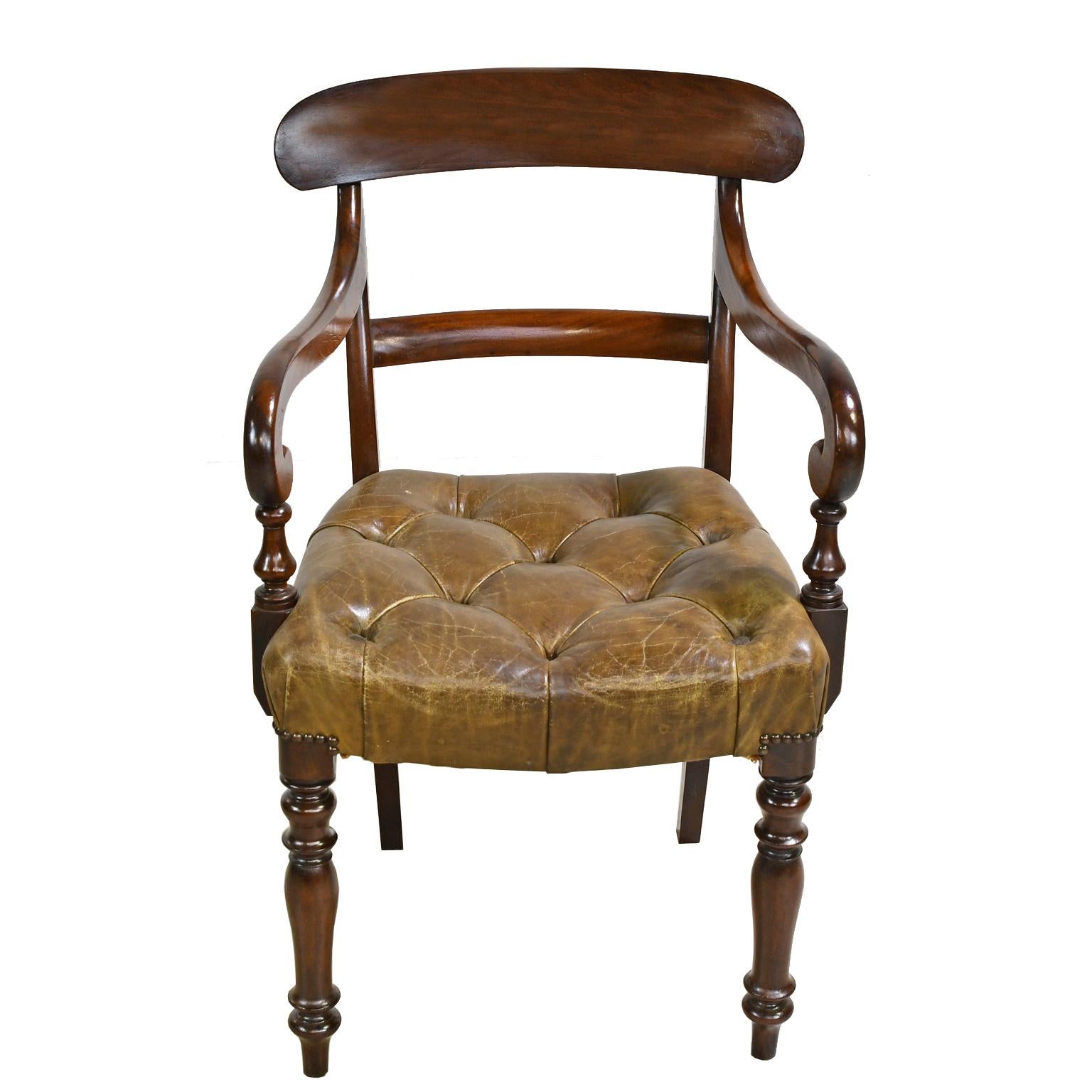 An early Victorian armchair in mahogany with curved top rail, scrolled arms, turned front legs and saber back legs. Seat is upholstered in a tufted, beige/camel-colored leather with brass nailheads. England, circa 1840. Note: There are a pair of