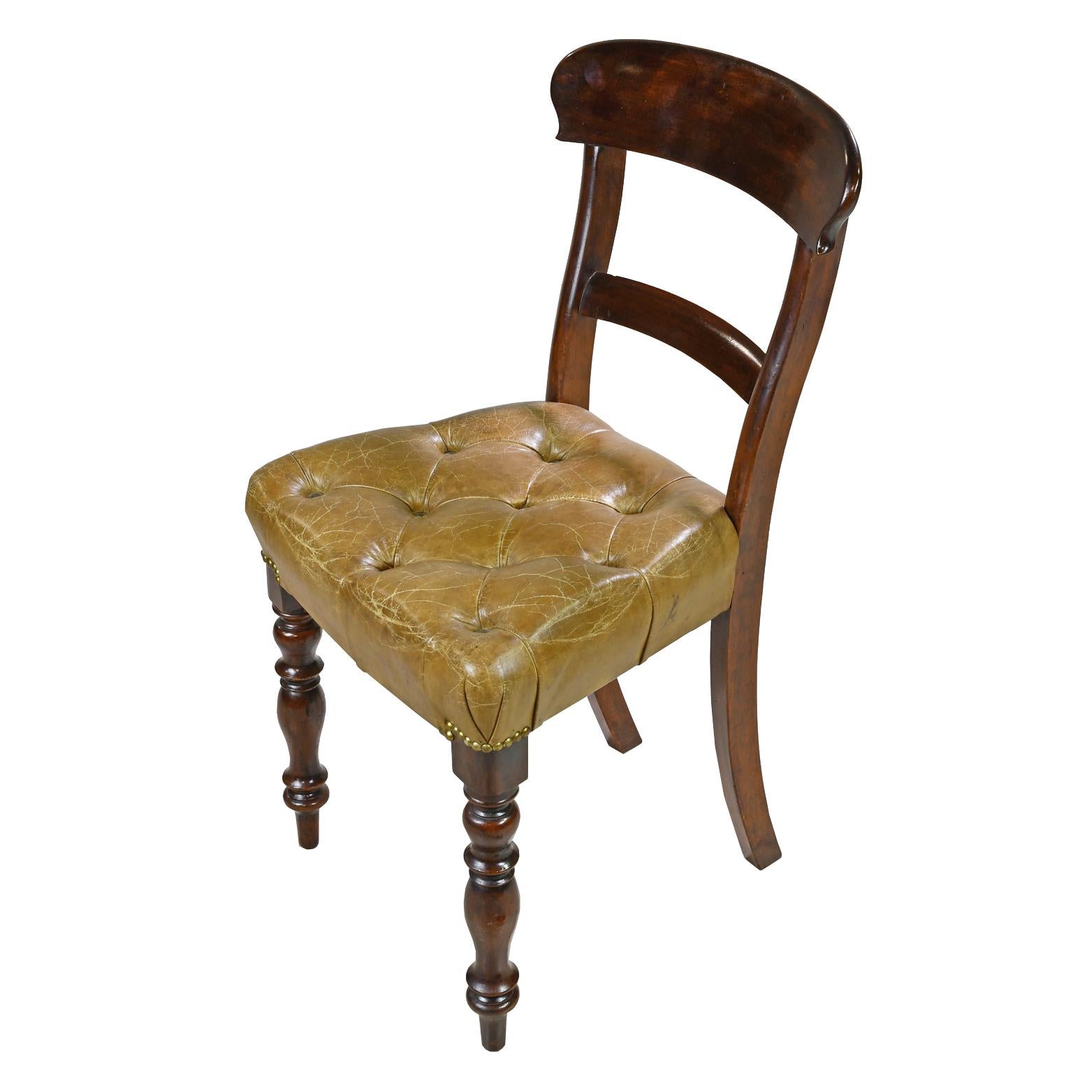 An early Victorian side chair in mahogany with curved top rail, and raised on turned front legs and saber back legs. Seat is upholstered in a tufted, beige/camel-colored leather with brass nailheads, England, circa 1840. Note: A pair of side chairs