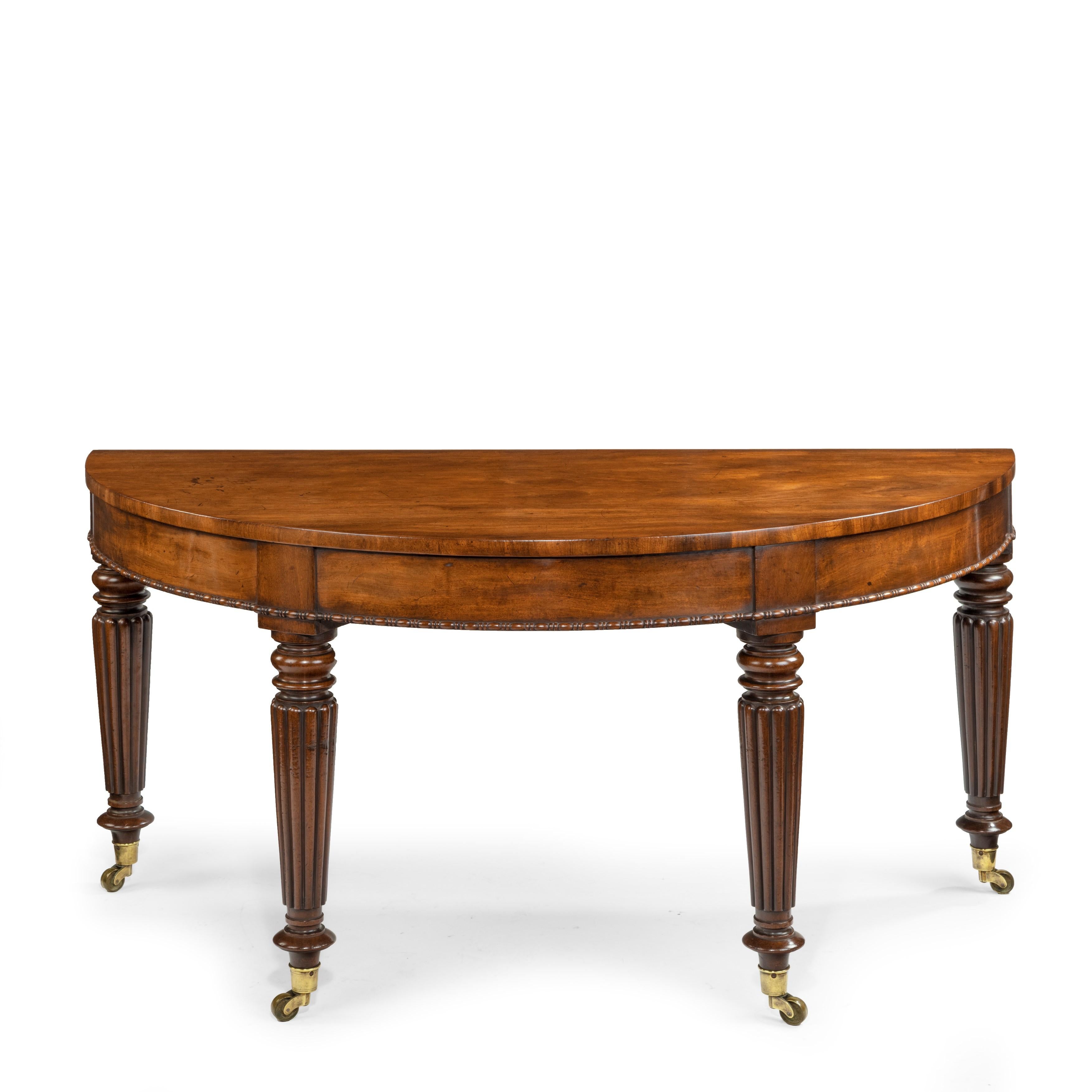 An unusual pair of early Victorian mahogany console tables attributed to Gillows, each demilune top set above four tapering, reeded and turned legs, the frieze decorated with bead and reel mouldings, on the original brass castors, English, 1840.
 