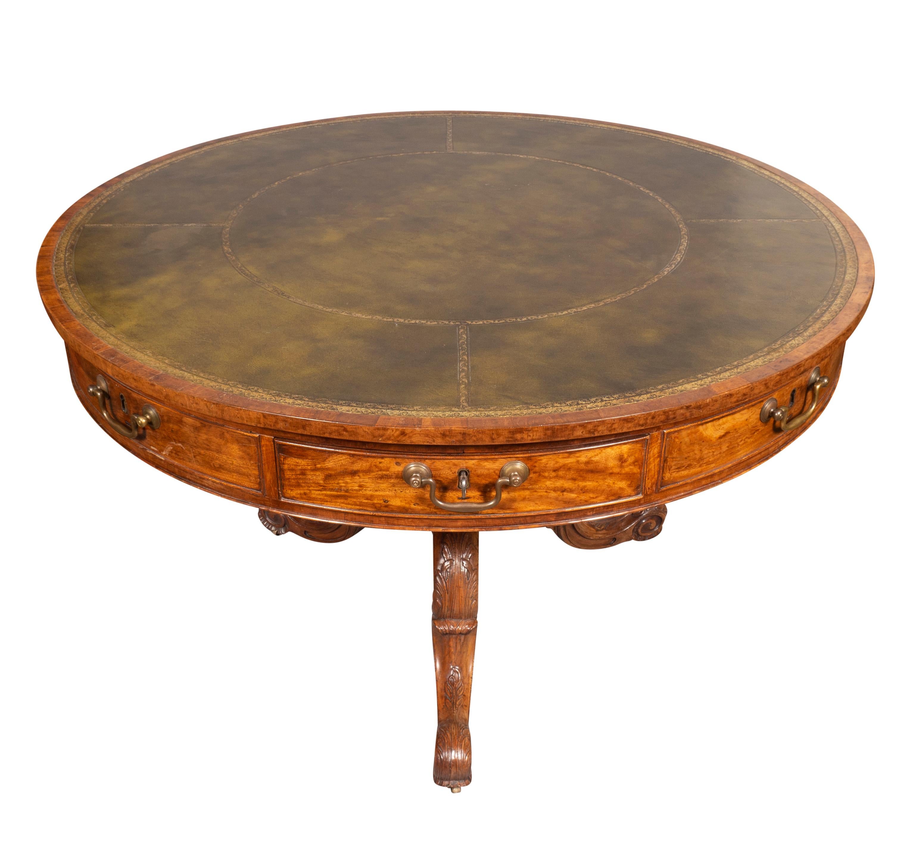 With circular top with inset tooled green leather and banded border over drawers with bail handles. The carved base with turned support and three carved cabriole legs and ending on scroll feet.