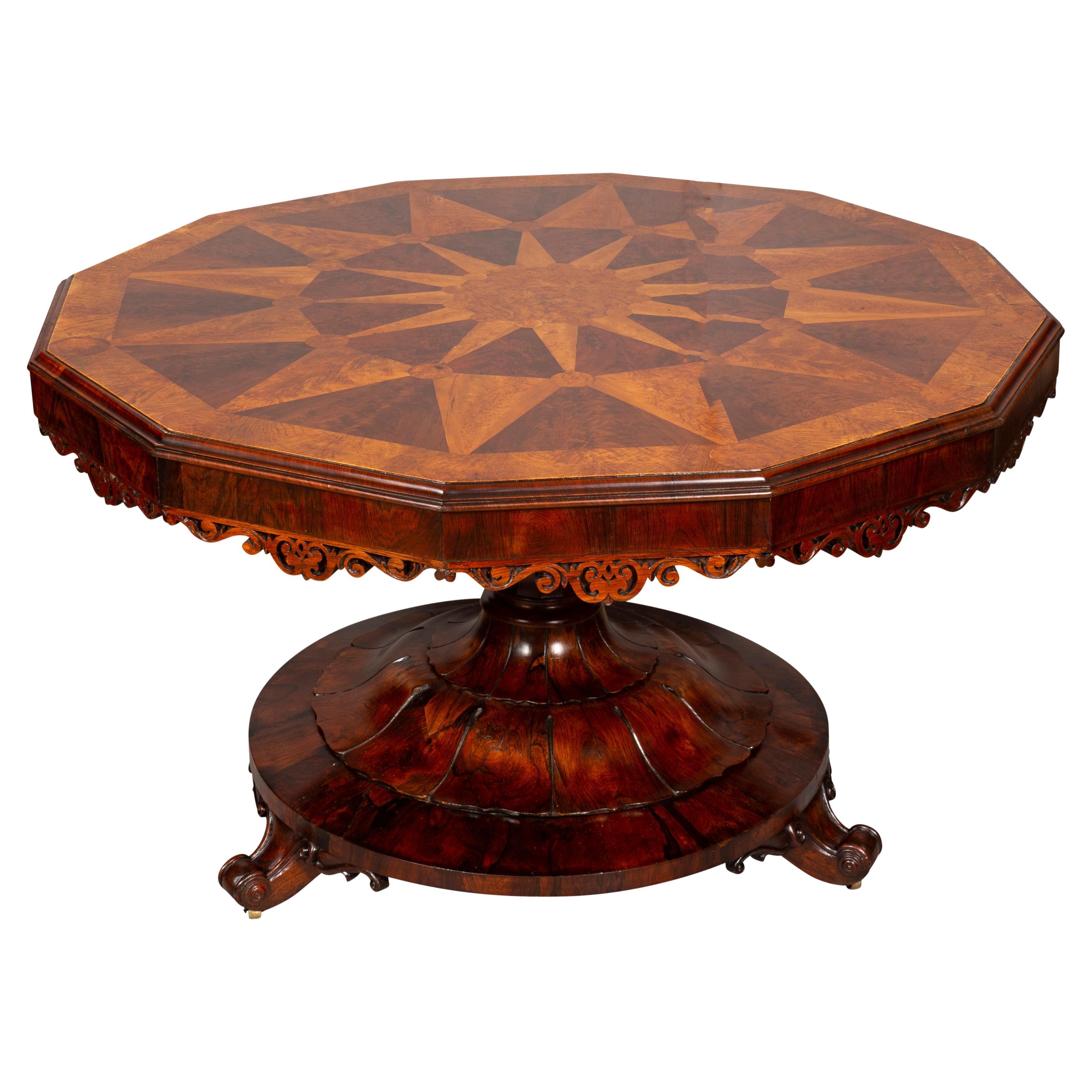 Twelve sided dodecagon hinged top with elaborate sunburst central inlay with outer band sunburst with elm outer banding, conforming apron with carved details, on a inverted vase support and circular plinth base, carved. 
French feet.