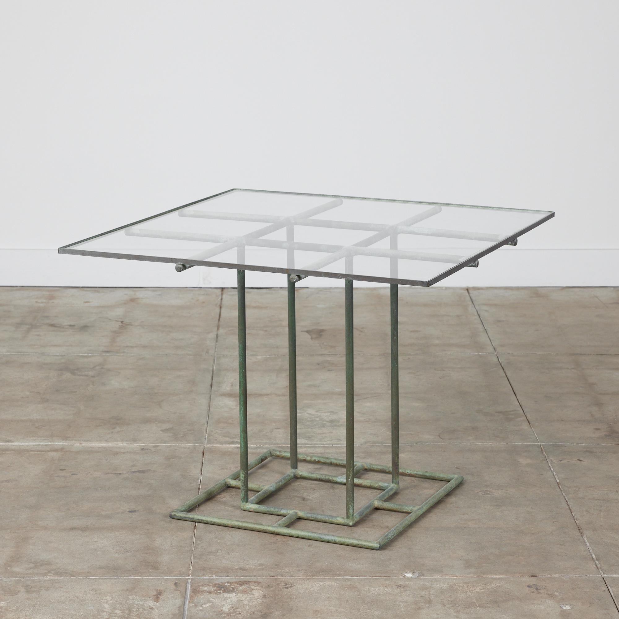 Square patio table designed by Walter Lamb from the late 40s or early 50s, either predating or from the early years of his work with Brown Jordan. The table has a glass table top that rests on a a tubular patinated bronze base. Its subtle geometry
