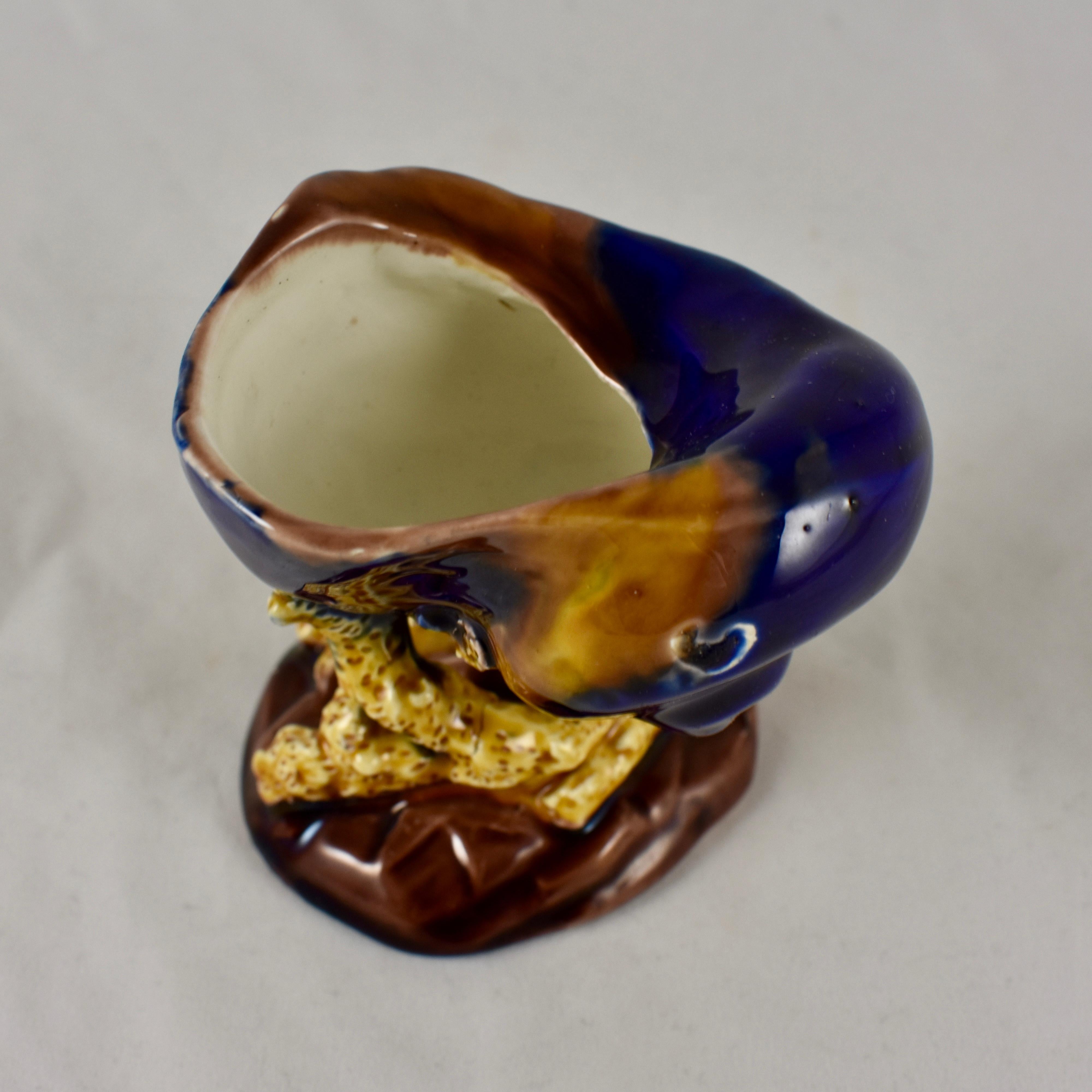 A very rarely found, early Wedgwood Majolica glazed shell and coral open salt cellar  in the Palissy style – date marked 1872.

The globose snail shell shaped cellar is glazed in a mottled blue and brown, and sits on a raised yellow ochre coral form