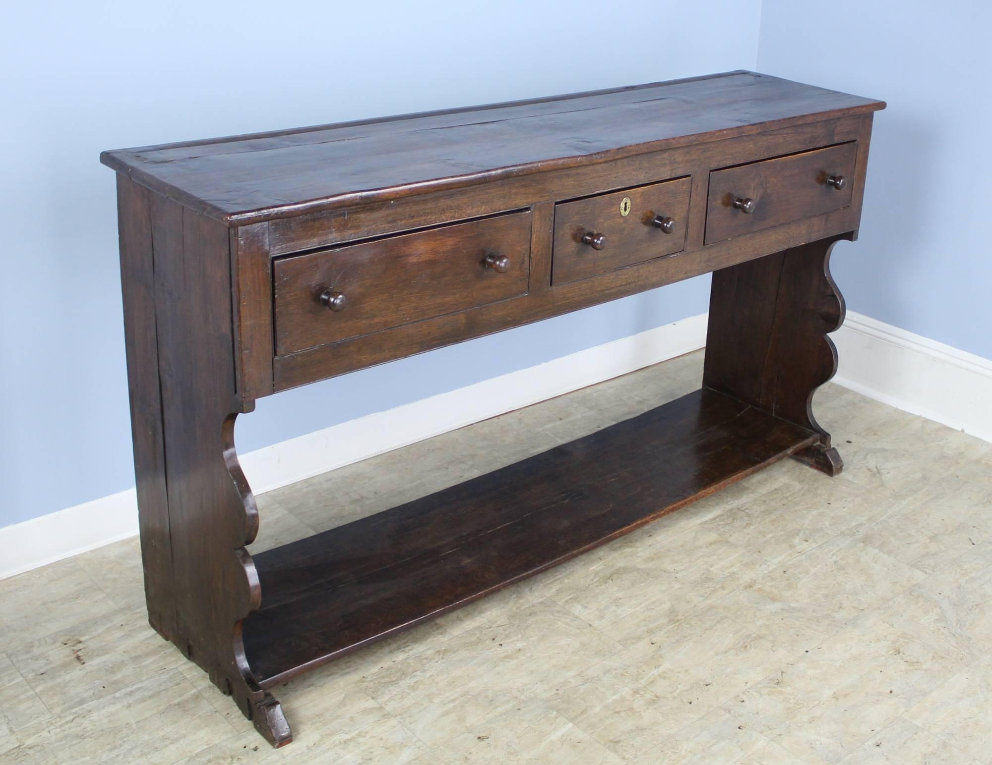 An early Welsh oak server with fancifully figured sides, roomy drawers and an extravagantly grained top. Lovely color and patina. The pot board below provides good storage.