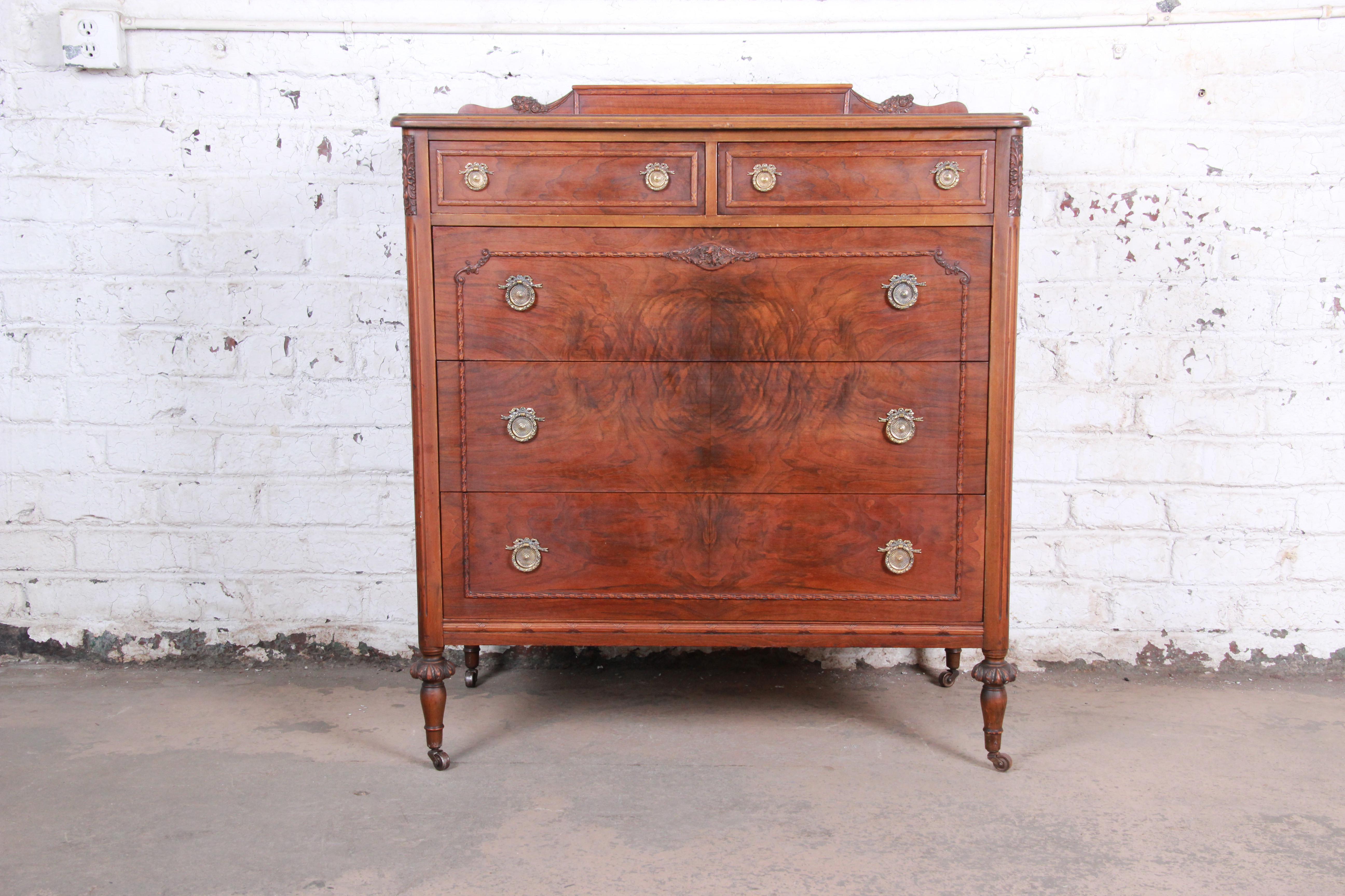 A gorgeous antique highboy chest of drawers by Widdicomb Furniture of Grand Rapids, circa 1920s. The dresser features stunning burled walnut wood grain and nice carved wood details. It offers ample storage, with five dovetailed drawers. The chest is
