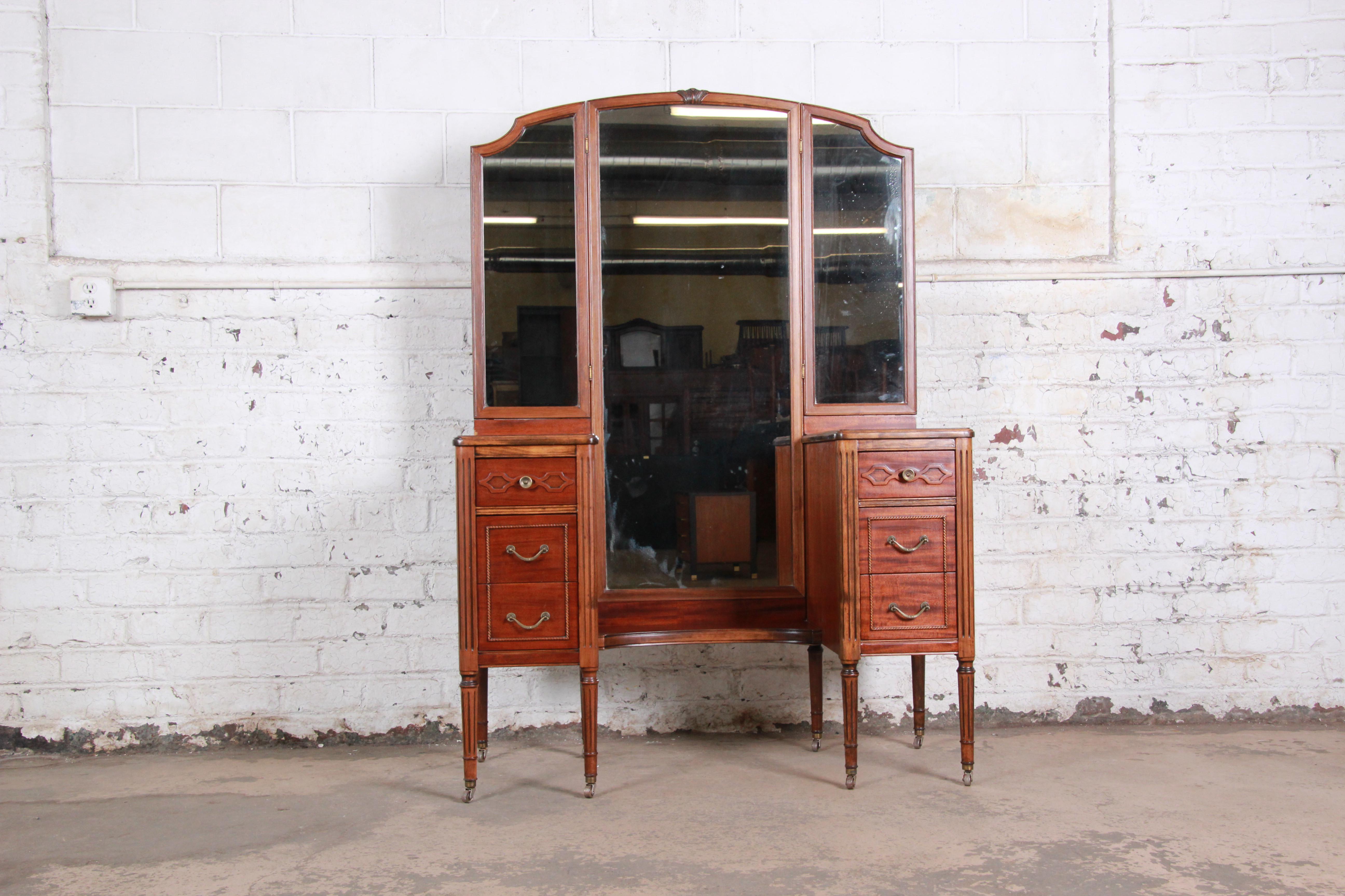 A gorgeous antique mahogany vanity dresser with mirror by Widdicomb Furniture of Grand Rapids, circa 1920s. The vanity features beautiful mahogany wood grain, nice carved wood details, and a large tri-fold mirror. It offers good storage, with six