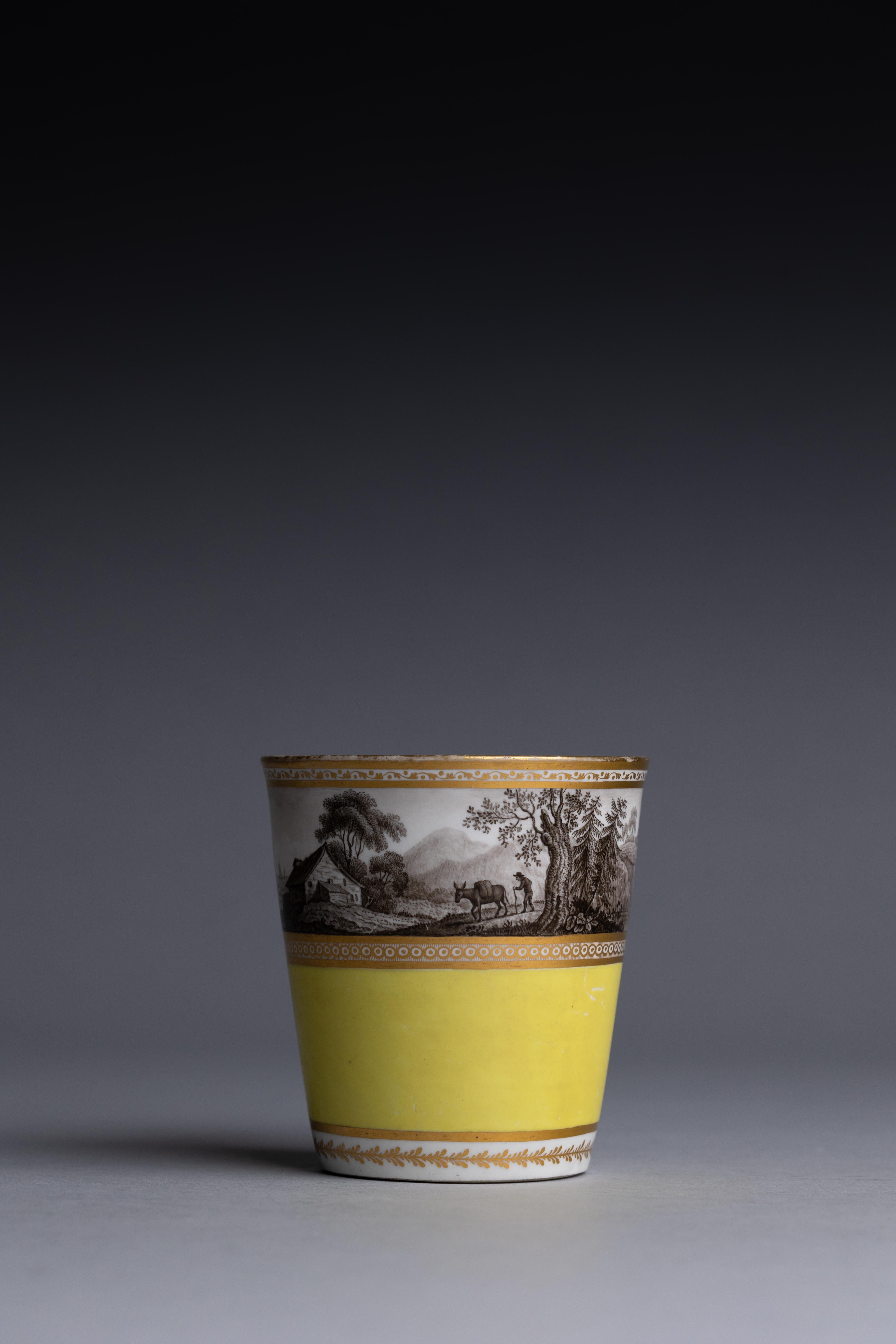 An early Worcester Flight & Barr bright yellow beaker with gilding and a finely painted sepia scene of a landscape. The scene, possibly painted by John Pennington, shows two figures looking at a ship sailing out to sea before a cliffside fort, a