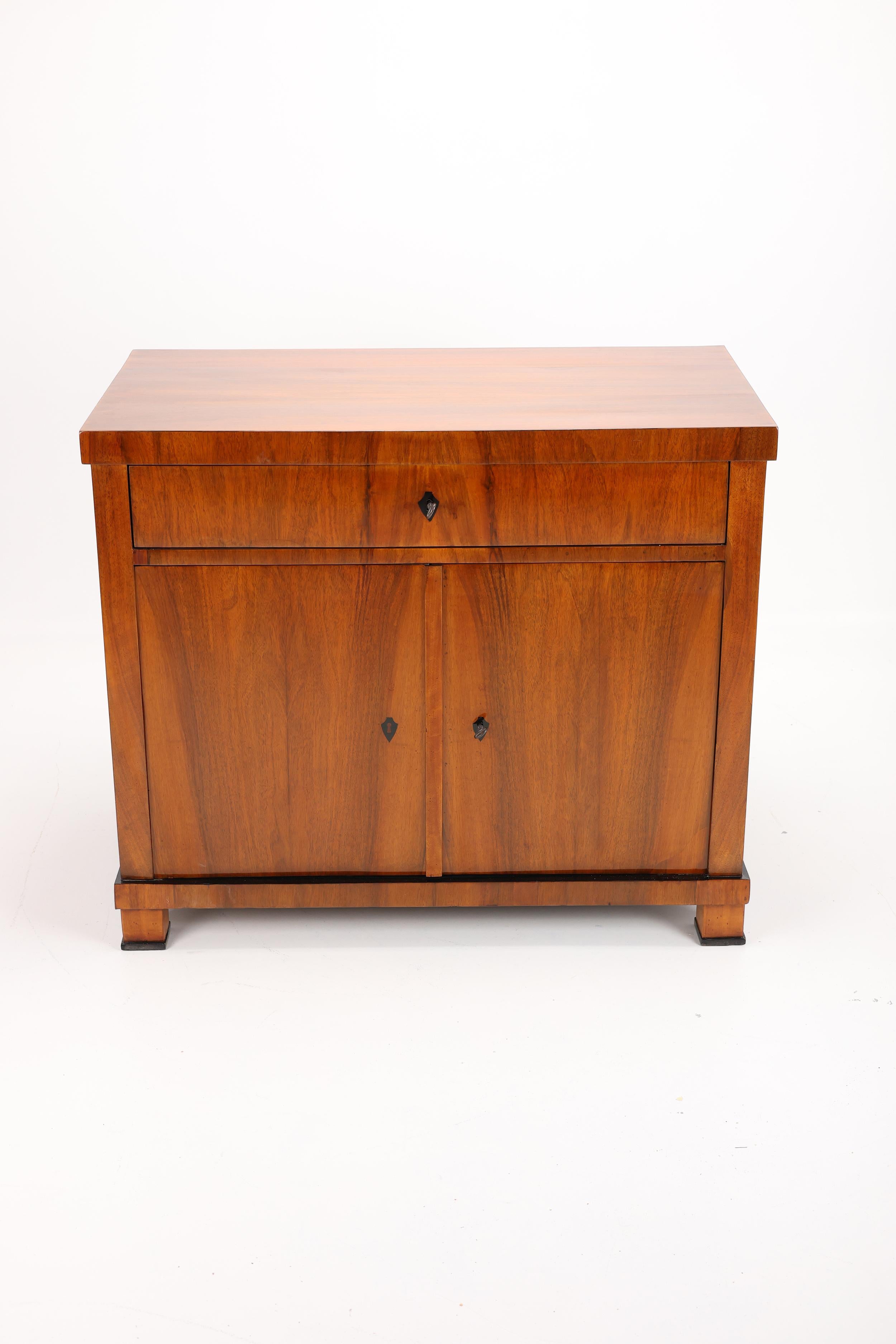 Questo squisito pezzo, realizzato all'inizio del XIX secolo, è uno splendido esempio di stile Biedermeier, originario della Germania meridionale tra il 1820 e il 1830. L'impiallacciatura di ottima fattura, con il suo armonioso motivo a venature,