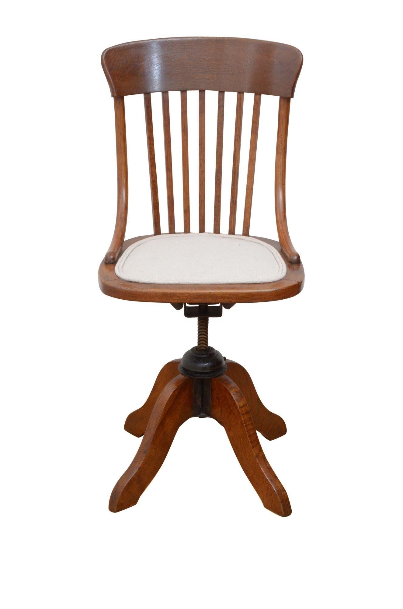 P0250 Unusual early 20th century, revolving and height adjustable chair in oak with shaped top rail, slatted back and newly upholstered seat with light colour top cover, standing on shaped, downswept legs. This antique chair is in home ready