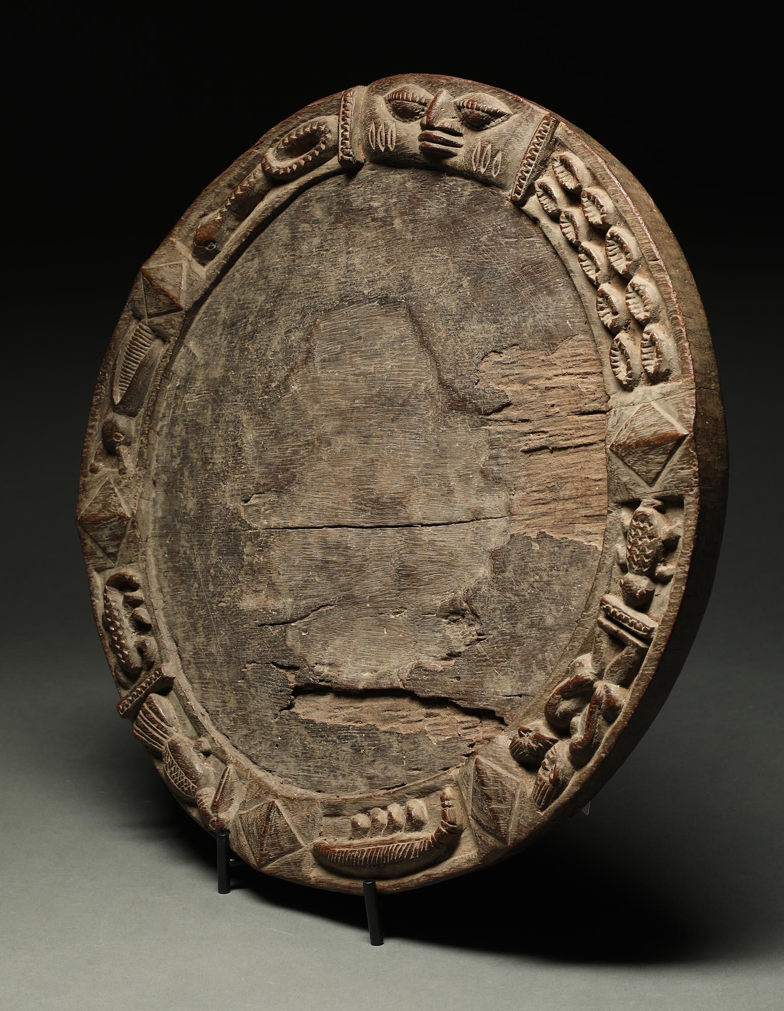 Very early large Yoruba divination board, a classic form round board with face at top, figures, couples, snakes, cowrie shells and other items around the edge of the board. Heavy wood, early 20th century, Nigeria. Areas of erosion and wear in center