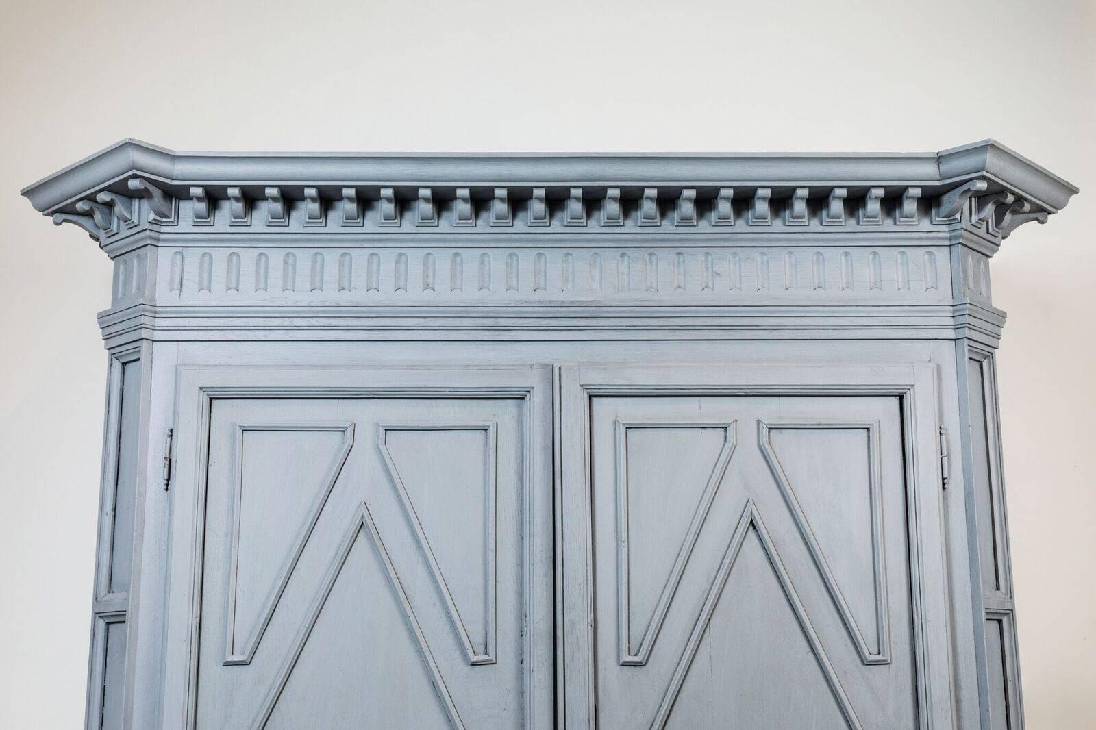 c. 1810, clipped corner, deux corp cabinet featuring a richly carved, overhanging, toothed cornice. The whole, newly painted in a matte, steel blue.