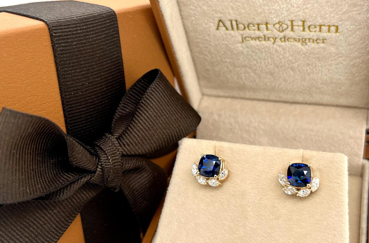 These stud earrings are crafted from 18kt yellow gold and feature cushion-cut Ceylon sapphires at their centers. The vivid blue hue of the sapphires adds a pop color, while marquise-cut diamonds surrounding them enhance the overall design with their