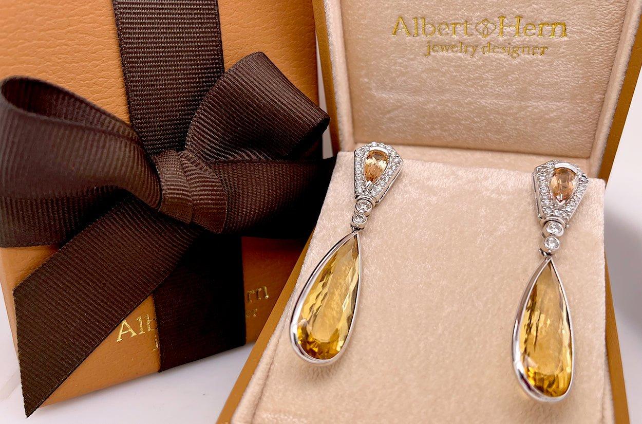 These dangle earrings exude timeless elegance with their 18kt white gold setting, featuring two radiant citrine pear-shaped gemstones that gracefully catch the light. Complementing the citrines are two precious topaz gems, adding a touch of