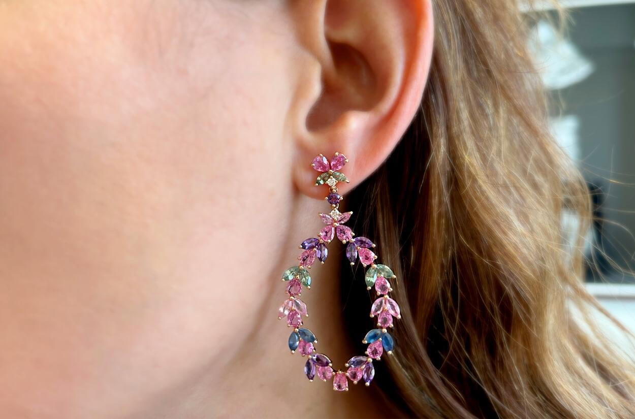 Exquisite dangle earrings crafted in the lustrous embrace of 18kt rose gold, adorned with resplendent pear-shaped pink sapphires resembling celestial tears, gracefully complemented by marquise-cut sapphires and amethyst gems and diamonds, creating a