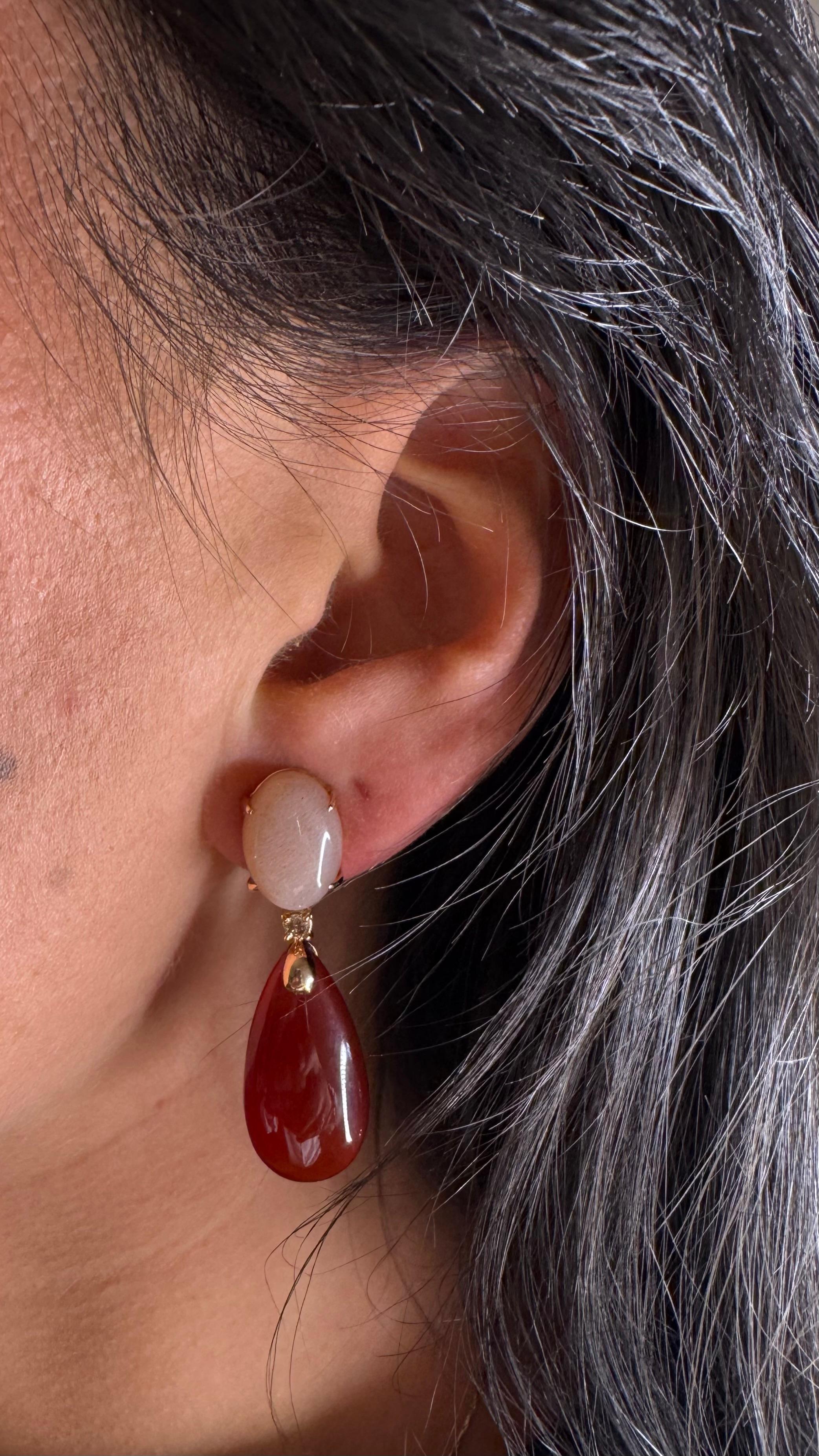 Orecchini peach moonstone cognac diamonds red Agathe. 

Questo bellissimo paio di orecchini presenta una pietra di luna color pesca a forma di cabochon montata su una gruccia articolata in oro rosa 18 carati. È separato dall'Agathe rosso da un