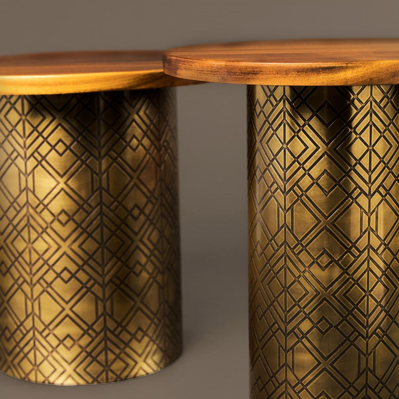 La table d'appoint Earth Prints 7A présente un plateau rond en bois massif de Dibetou, aux tons chauds et à la finition lisse, reposant sur une base cylindrique en laiton gravé à la patine dorée vieillie. Le motif géométrique finement gravé sur le