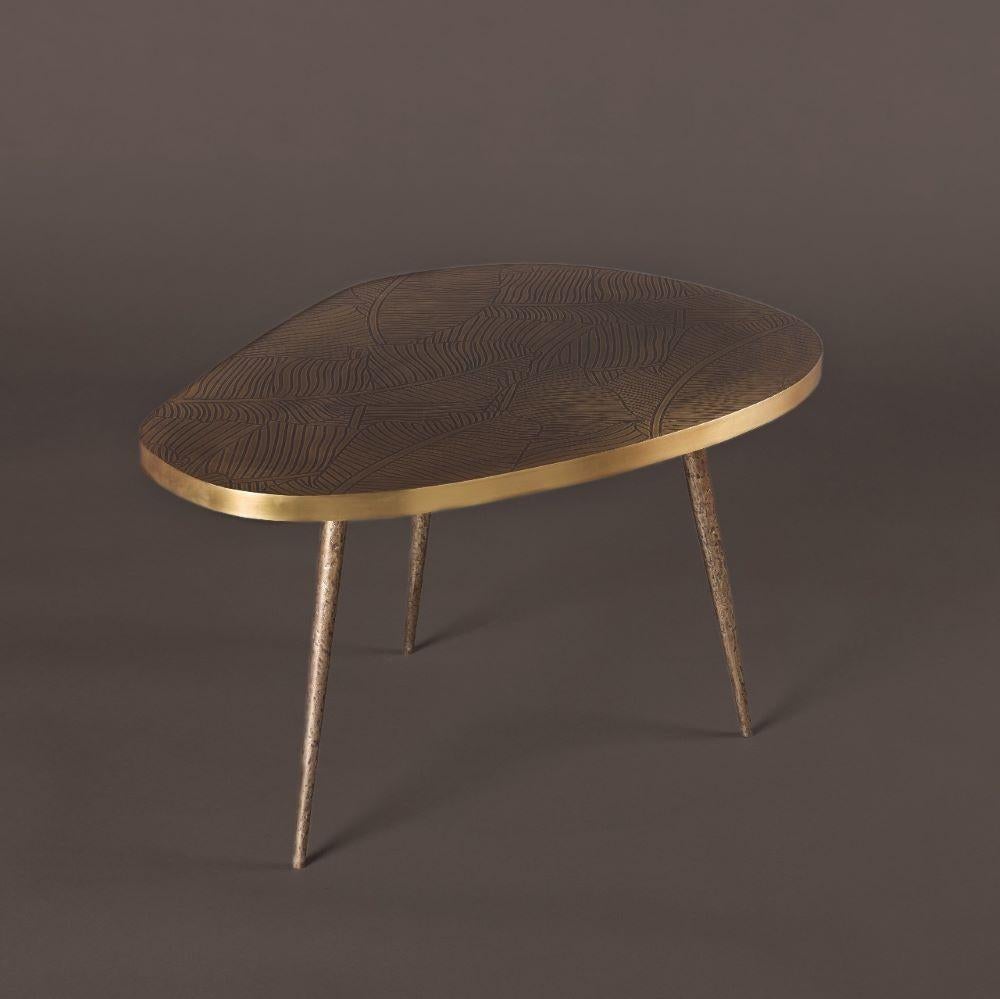 The Earth Prints 8 side table  features an asymmetrical top made of solid brass, hand-engraved in our workshop. The surface displays a flowing botanical pattern composed of interlacing lines, offering a rich, organic visual rhythm. A slightly