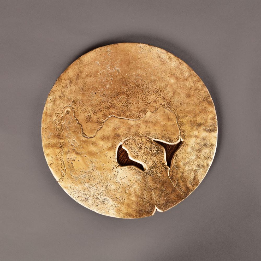 Earth Prints 10 est une table d'appoint combinant un plateau en laiton massif, coulé selon des techniques traditionnelles, avec une base cylindrique en placage de chêne. Le dessus présente un contour irrégulier aux bords adoucis, façonné par le
