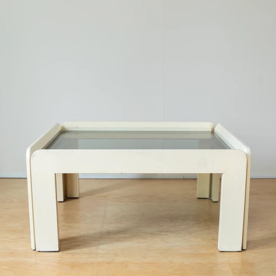 This is a low table with a modern design from Italy. The frame is made of wood with an ivory lacquer finish and has a slightly dark glass top.

The earthy colors and form give it a soft feel, but the glass top creates a contrast between the