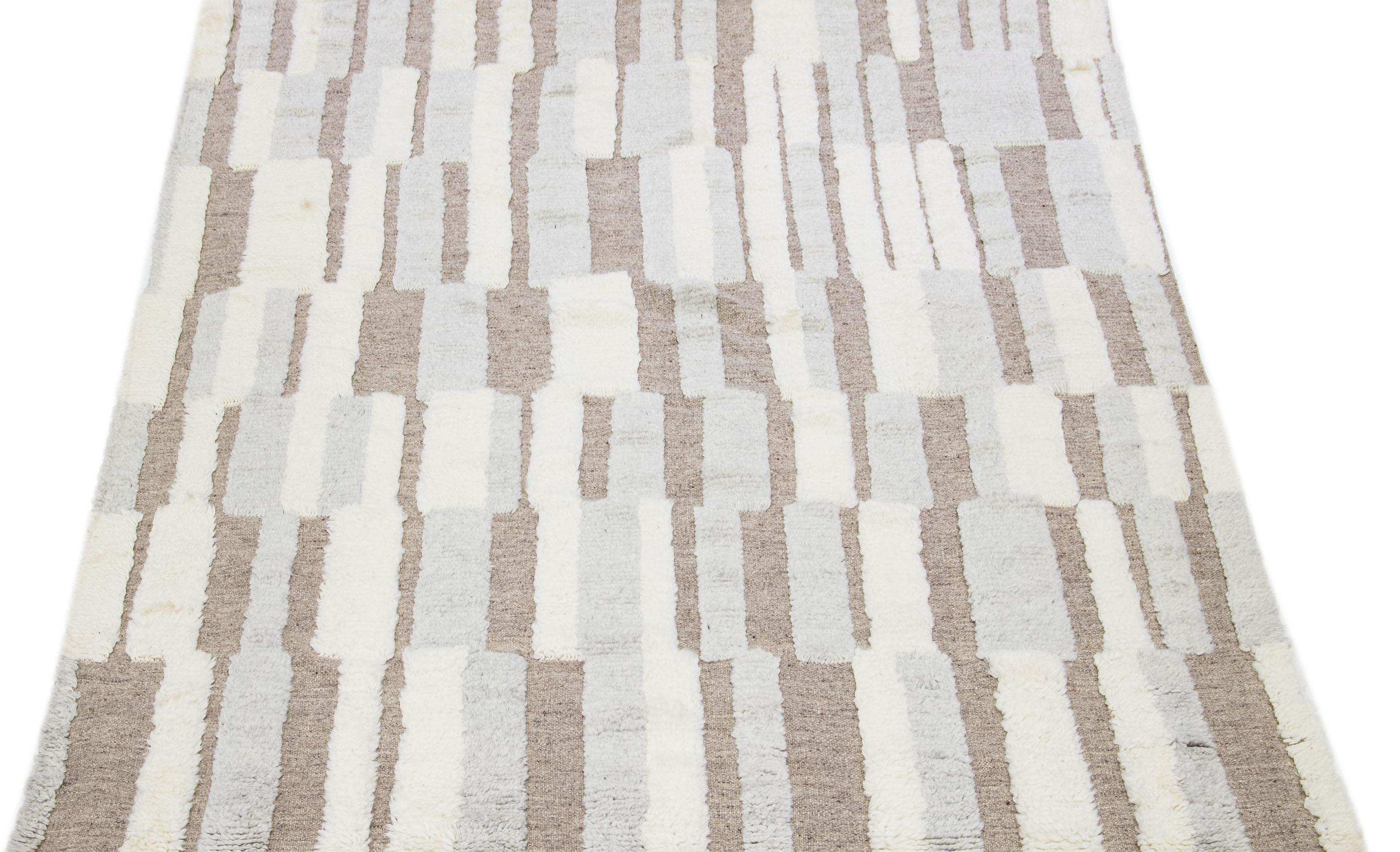 Ce tapis en laine a été habilement confectionné avec une attention méticuleuse aux détails. Il présente un motif marocain complexe, tissé avec brio dans de multiples nuances d'ivoire et de gris. Sa toile marron exquise ajoute un contraste