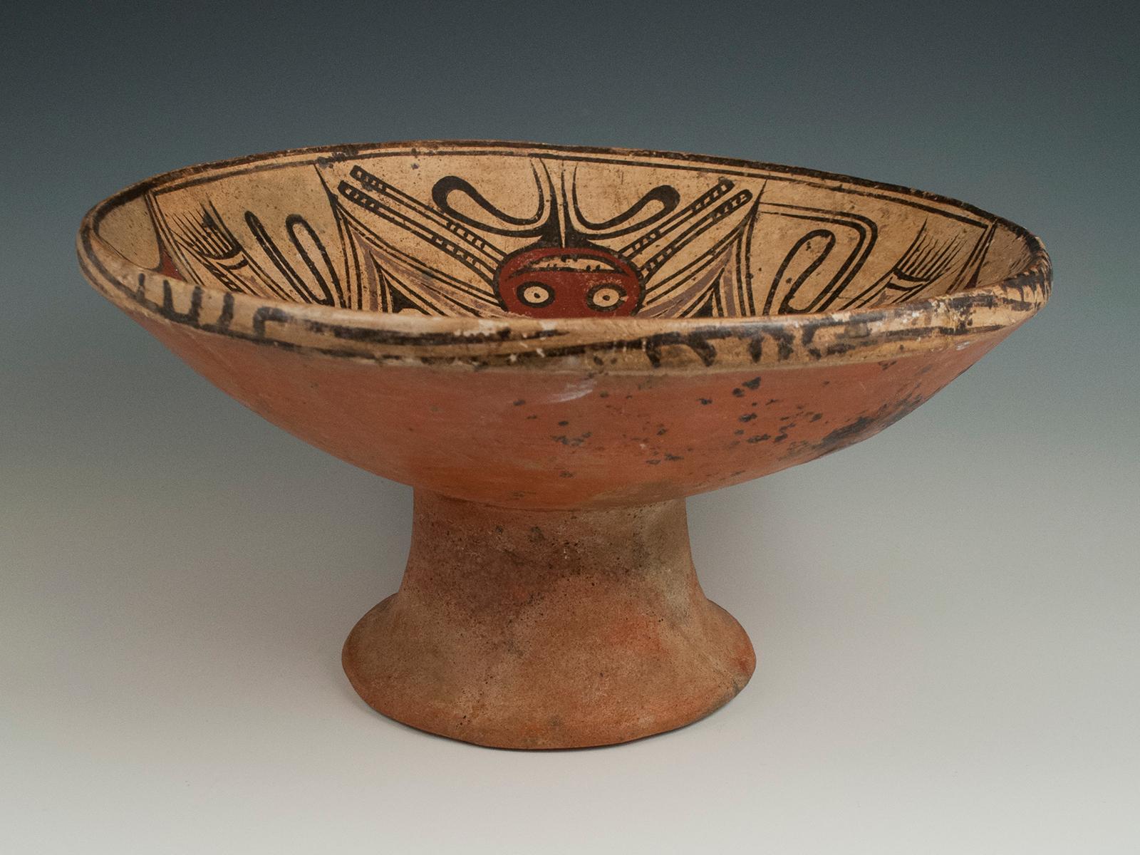 Earthenware bat pedestal dish, Coclé Culture, Panama

Earthenware dish on a low pedestal foot; the dish face is painted black, red and purple on a cream ground, each half of the bisected design depicting the mirrored image of a stylized bat. There