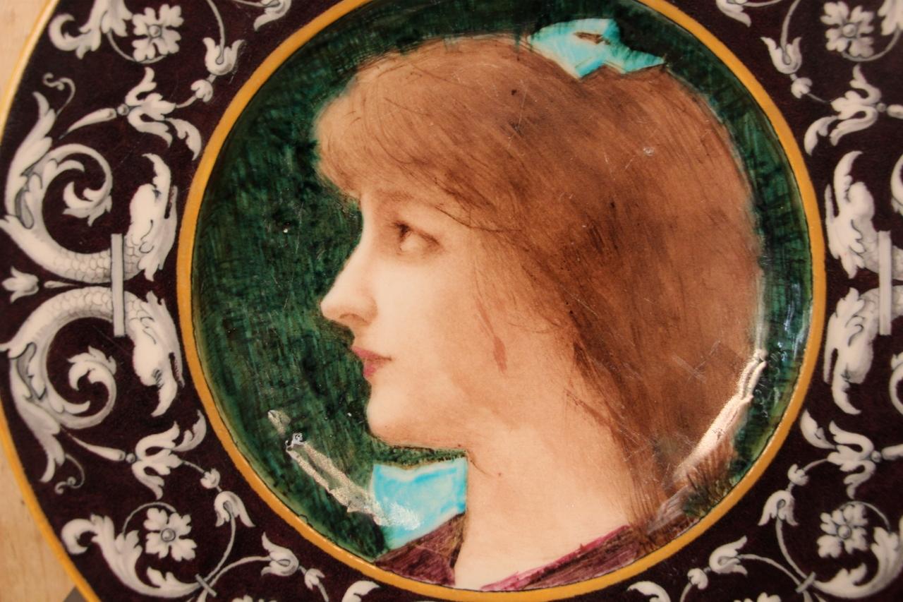 earthenware dish with polychrome enameled decoration depicting a young red-haired woman in profile, the margin decorated with a frieze of scrolls and dolphins on a brown background, signed on the back in very good condition, minimal scratches from