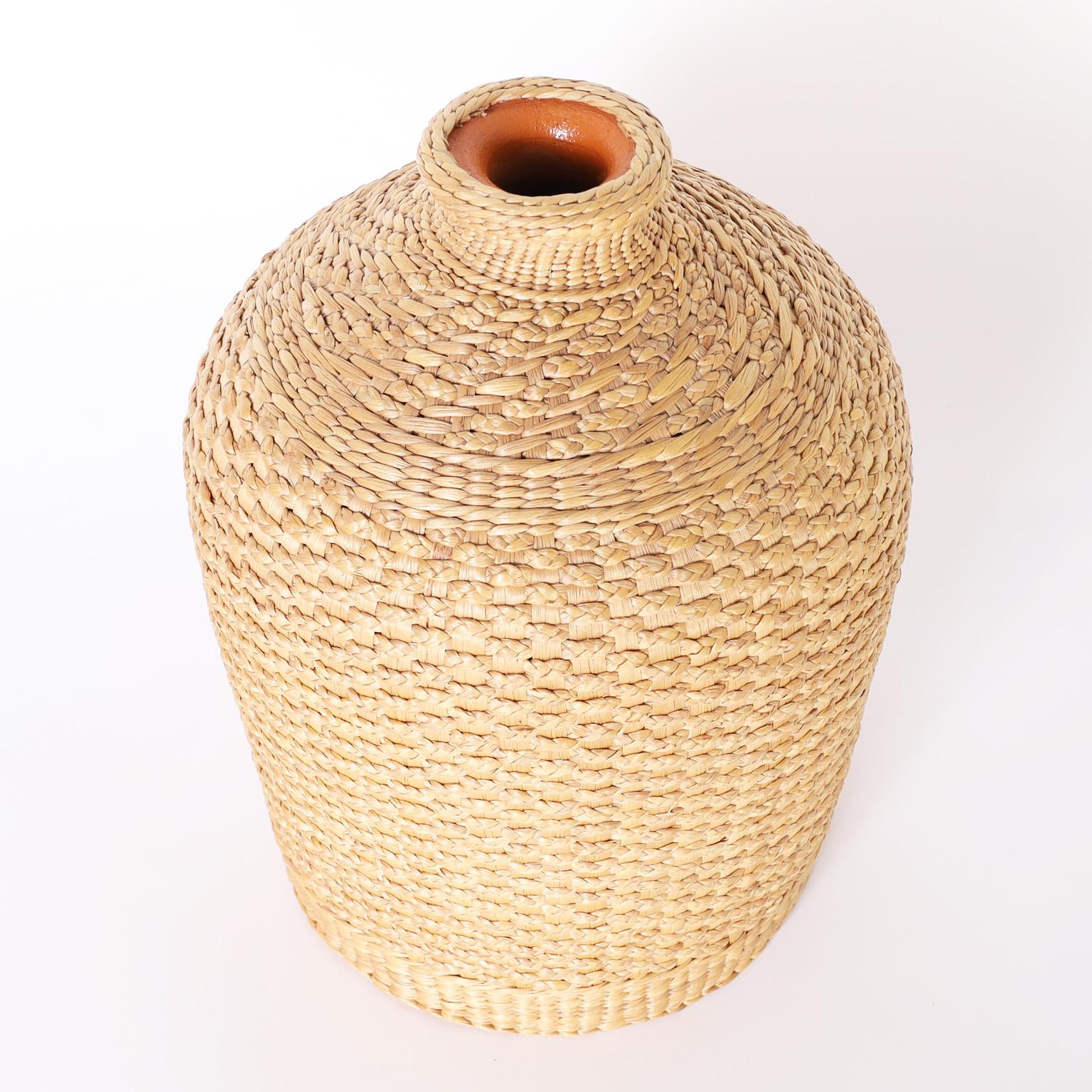 Unusual bottle or vase crafted in terra cotta with classic form and covered in ambitiously woven reed.