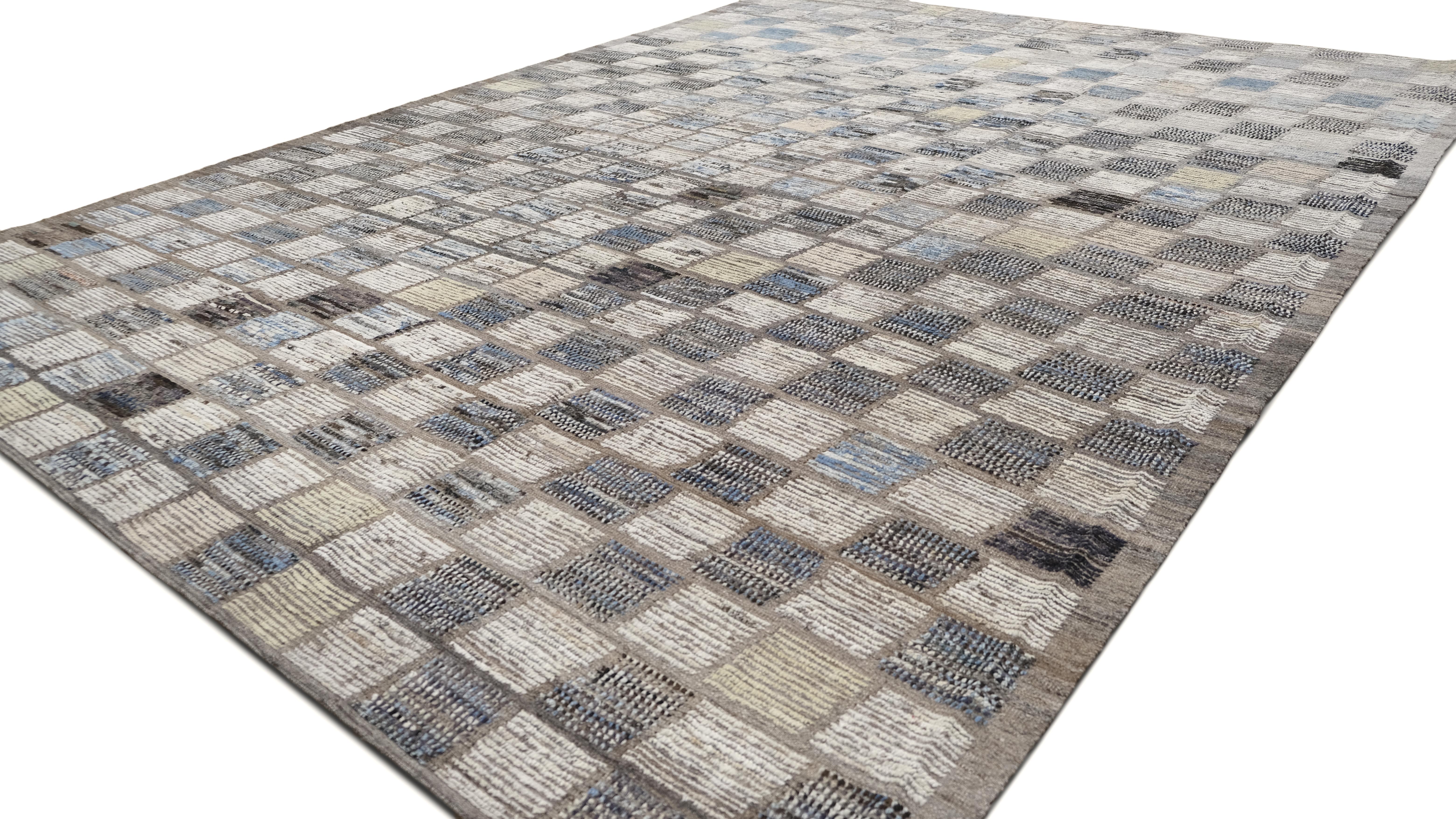 Dieser exquisite, handgeknüpfte Wollteppich zeichnet sich durch ein dynamisches Schachbrettmuster aus, das von einer strukturierten Anordnung zu einem eher abstrakten Layout übergeht. Die Mischung aus neutralen Beige- und sanften Blautönen sorgt für